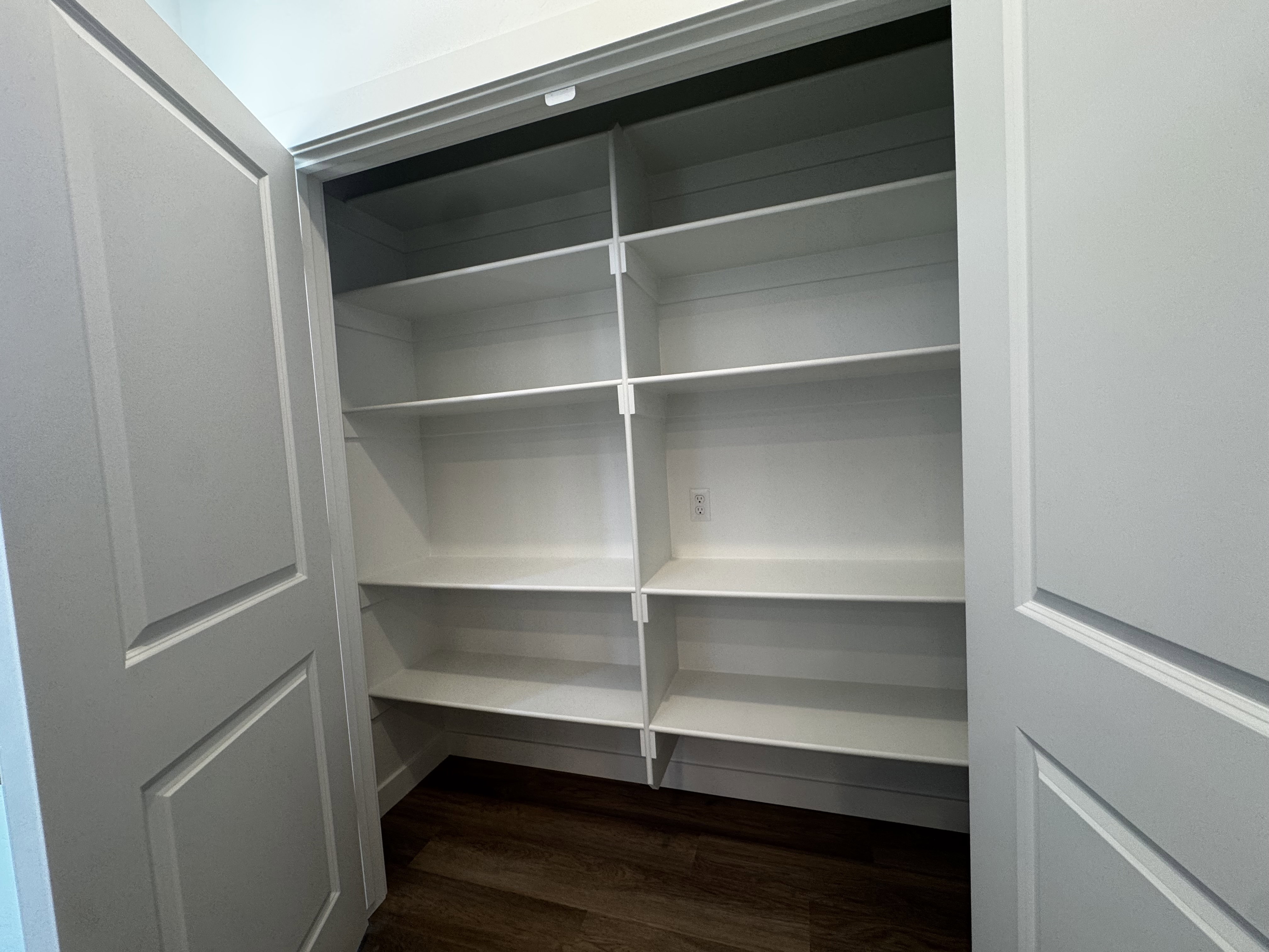 Spacious pantry featuring multiple white shelving units, paneled bi-fold doors, and wood-finish flooring