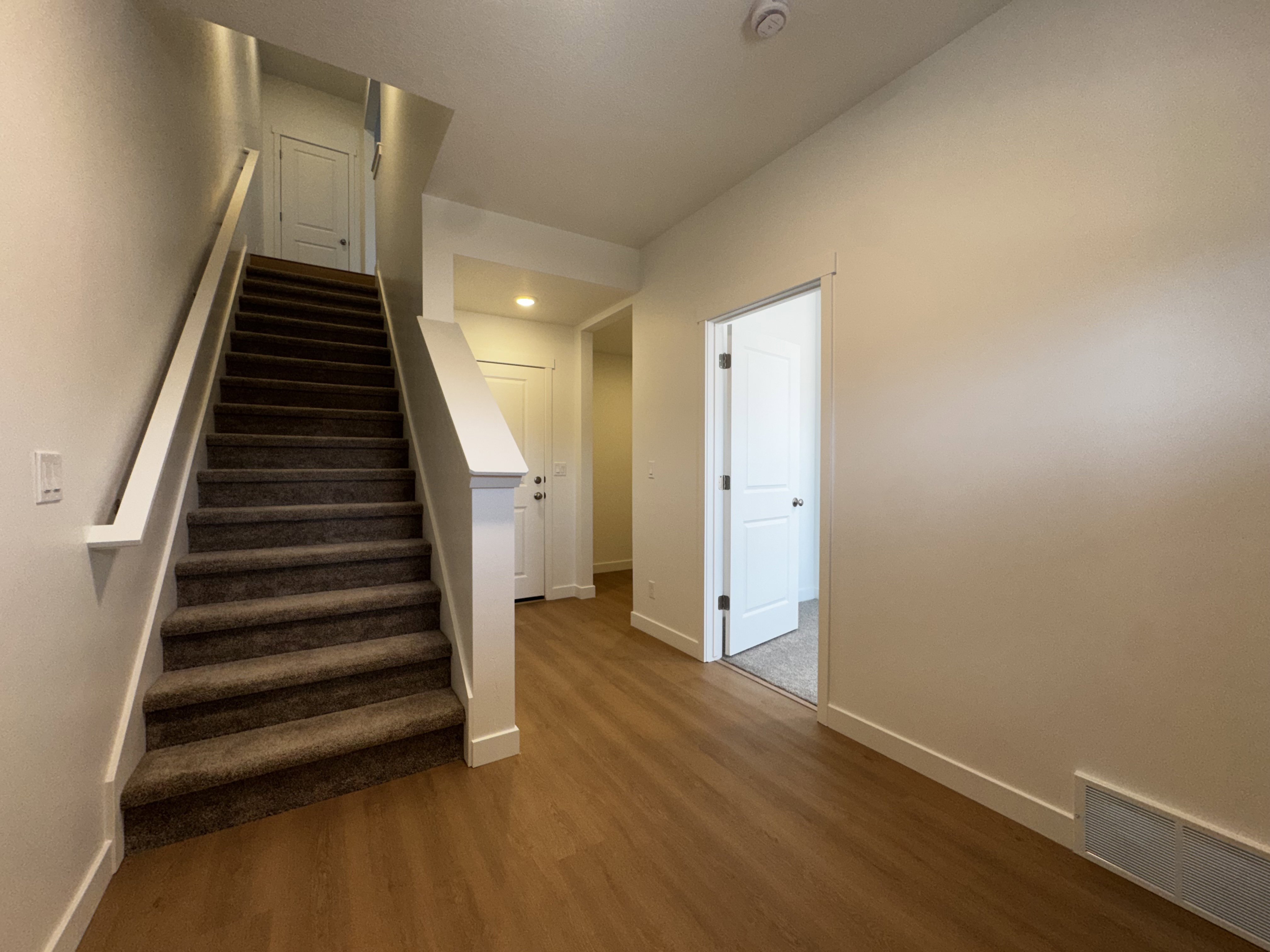 Carpeted staircase with white railing, wood-finish flooring, and white interior doors