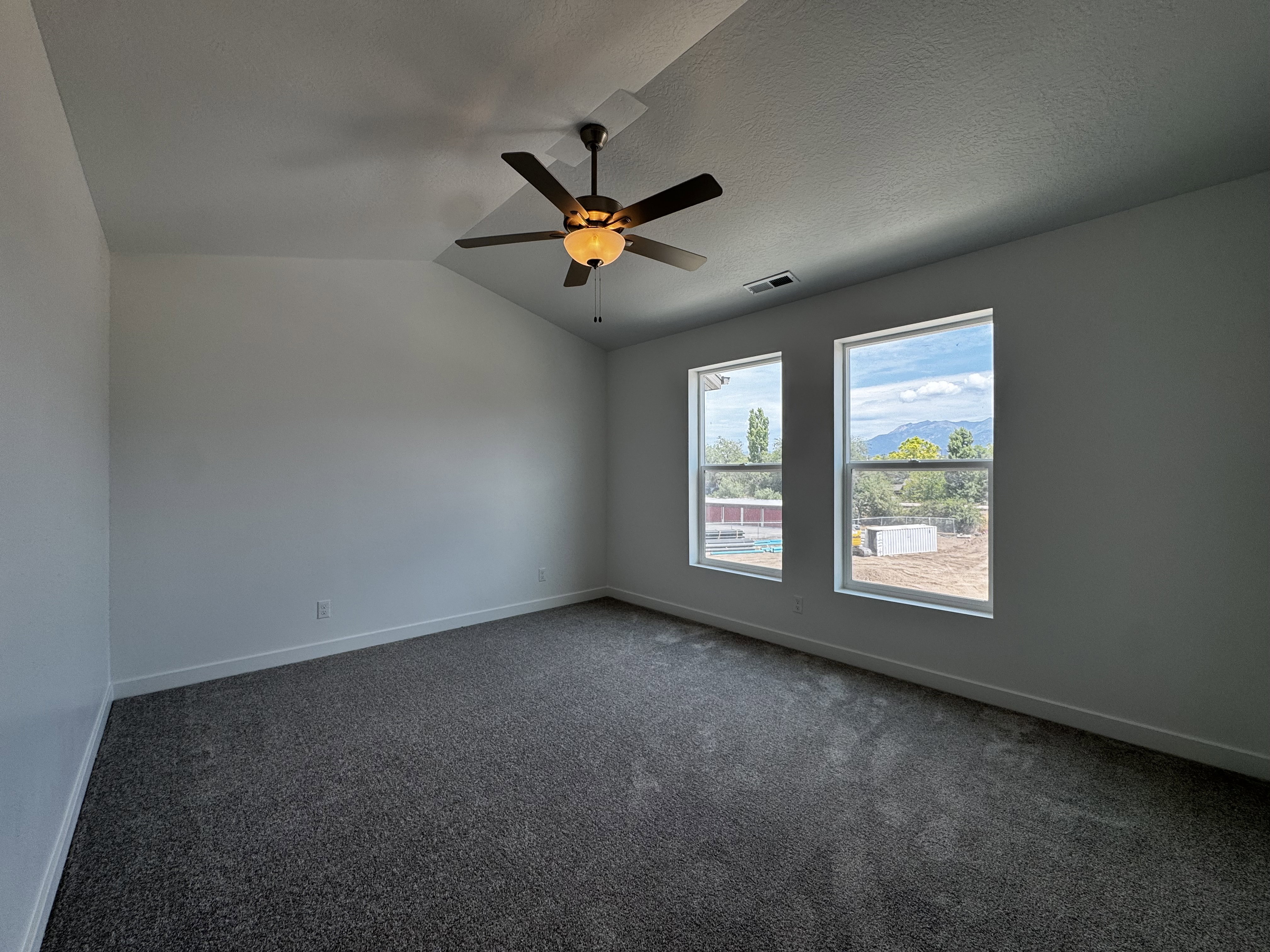 Room featuring a vaulted ceiling with a ceiling fan, two large windows, and wall-to-wall carpeting
