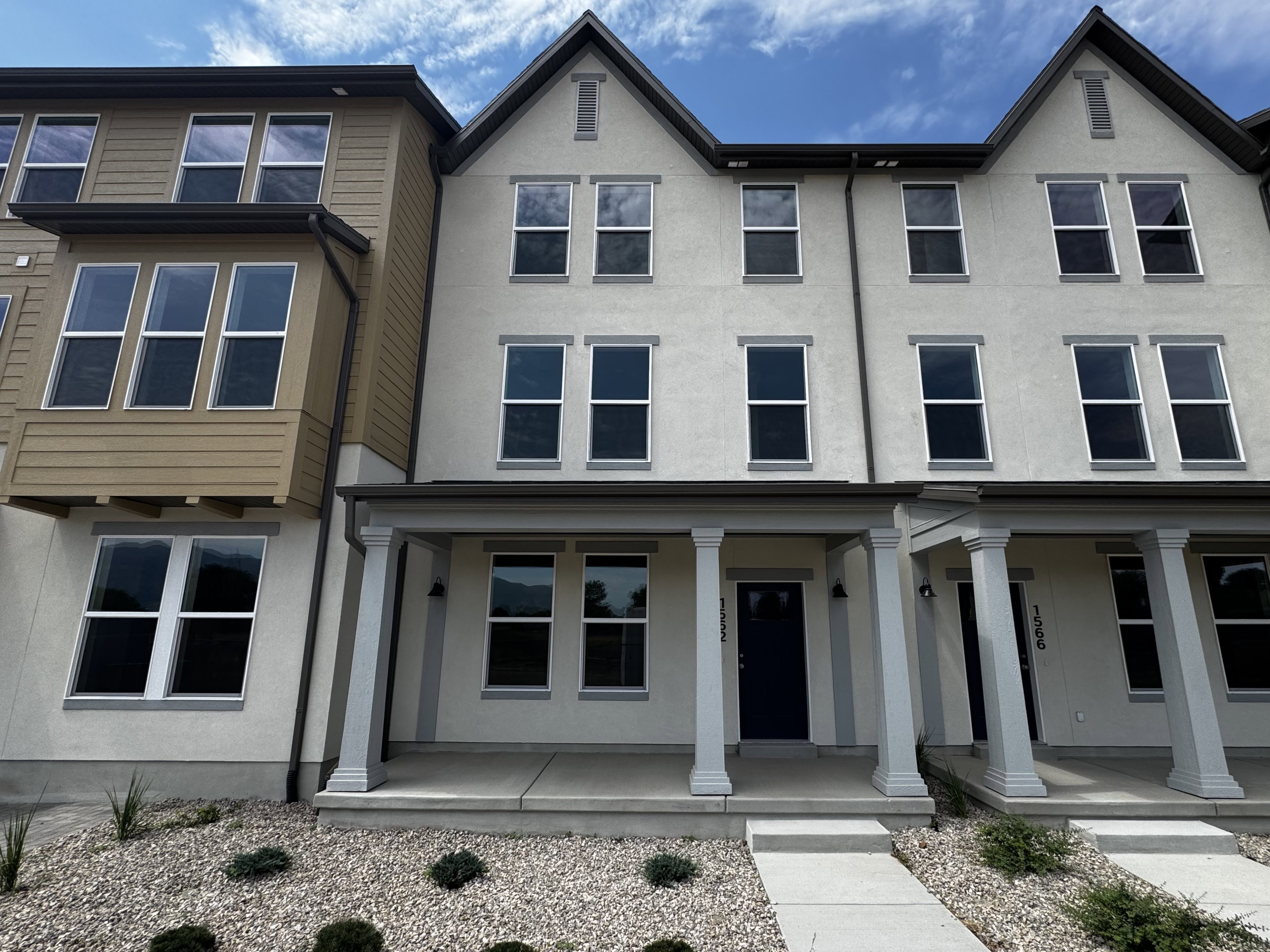 Multi-story townhome featuring a neutral stucco exterior, prominent bay window with horizontal siding, and an inviting covered porch
