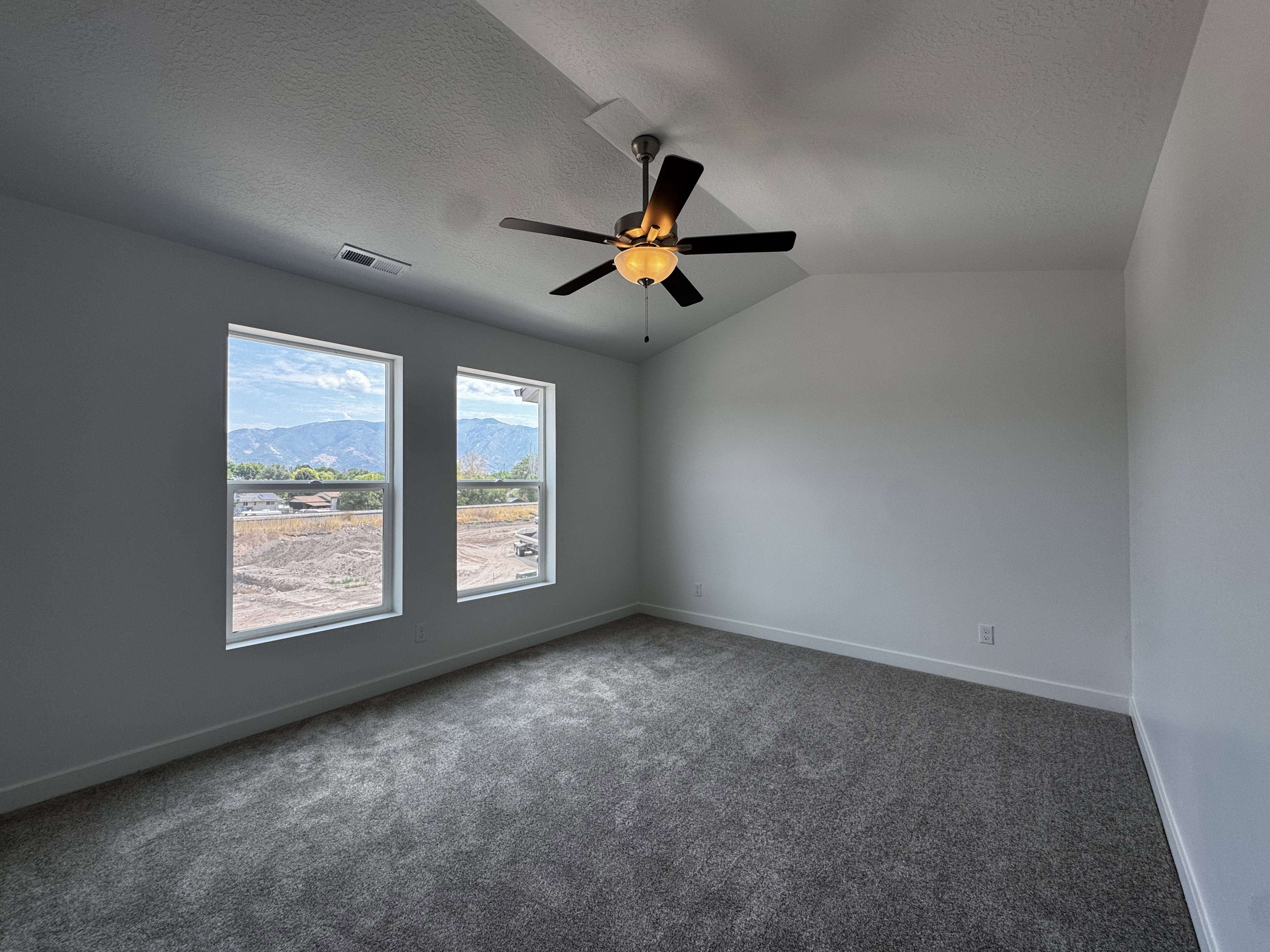 Room featuring two windows, a ceiling fan with integrated lighting, and vaulted ceilings