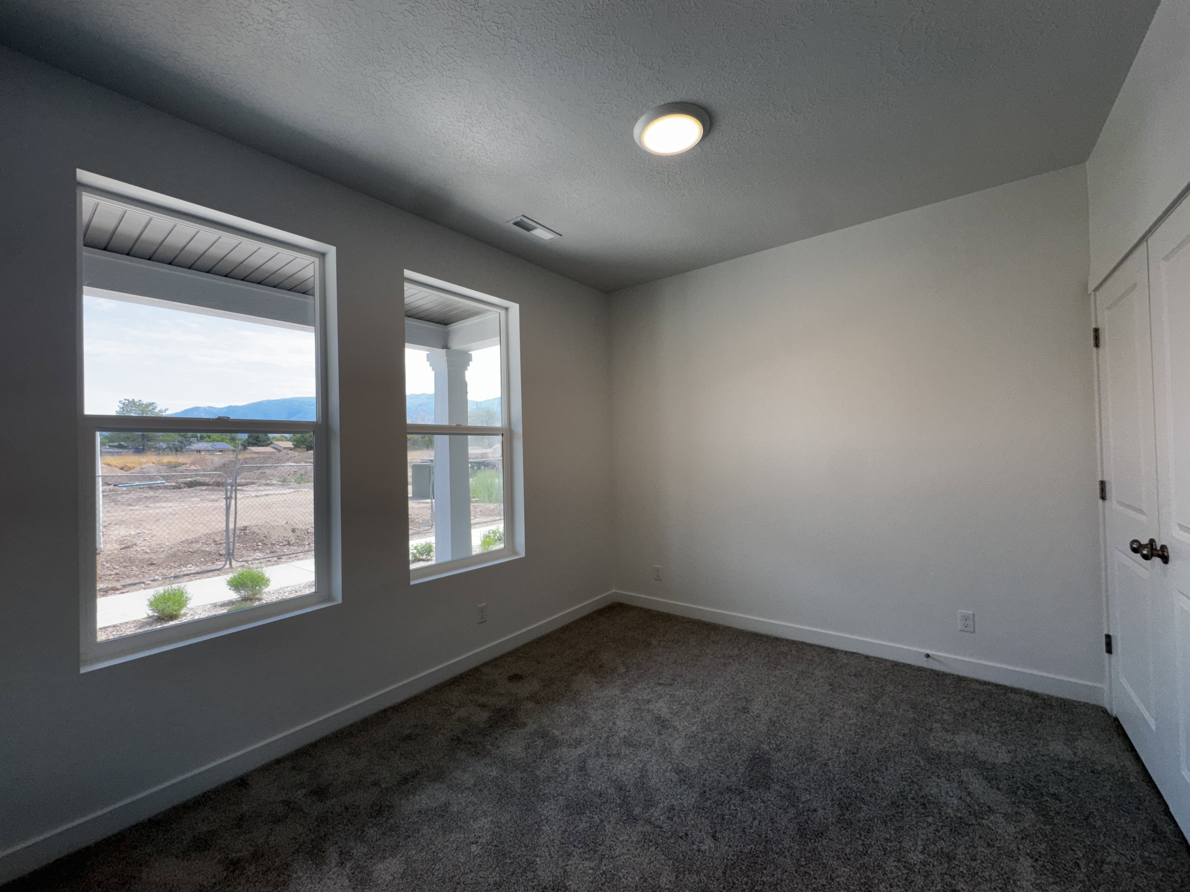 Room featuring two large windows, neutral-toned walls, and dark gray carpeting