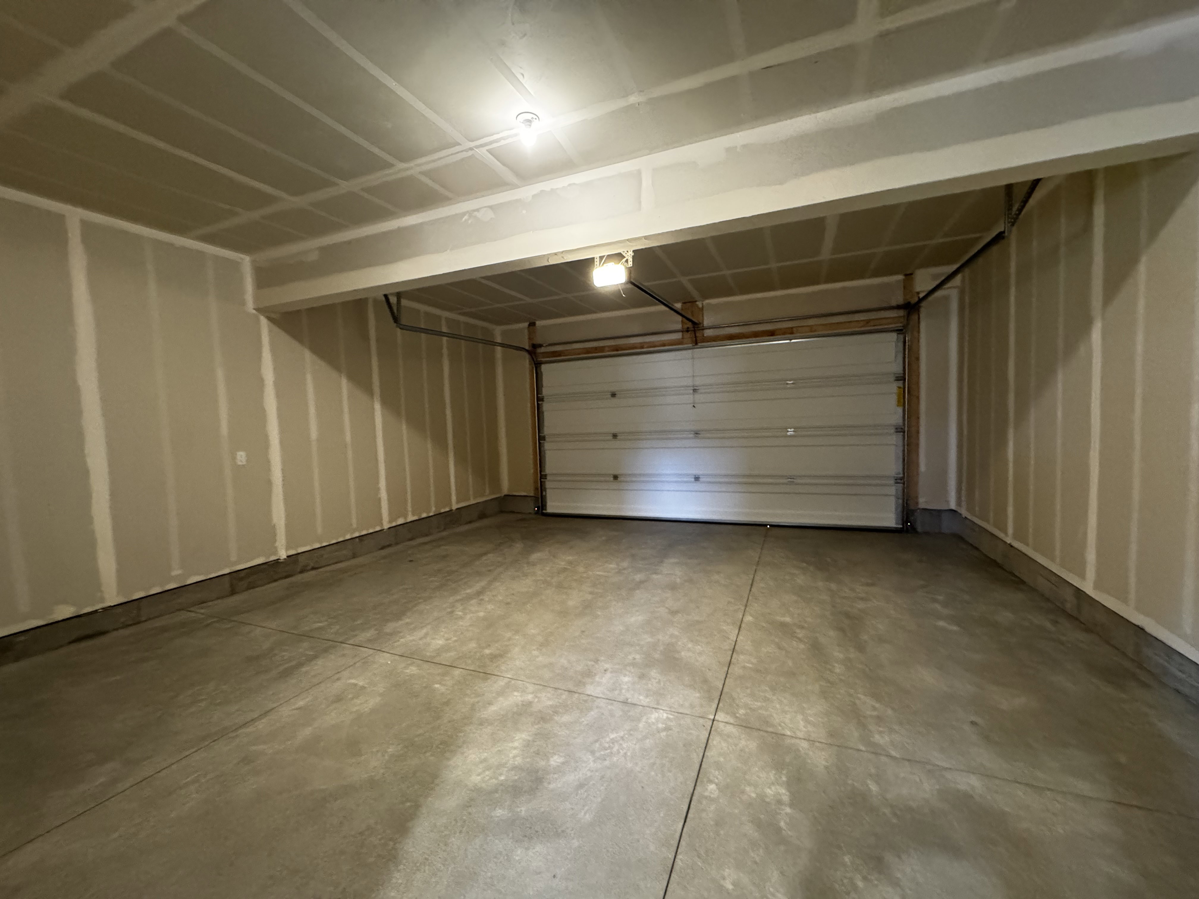 Spacious garage featuring a sectional overhead door, concrete flooring, and exposed ceiling joists