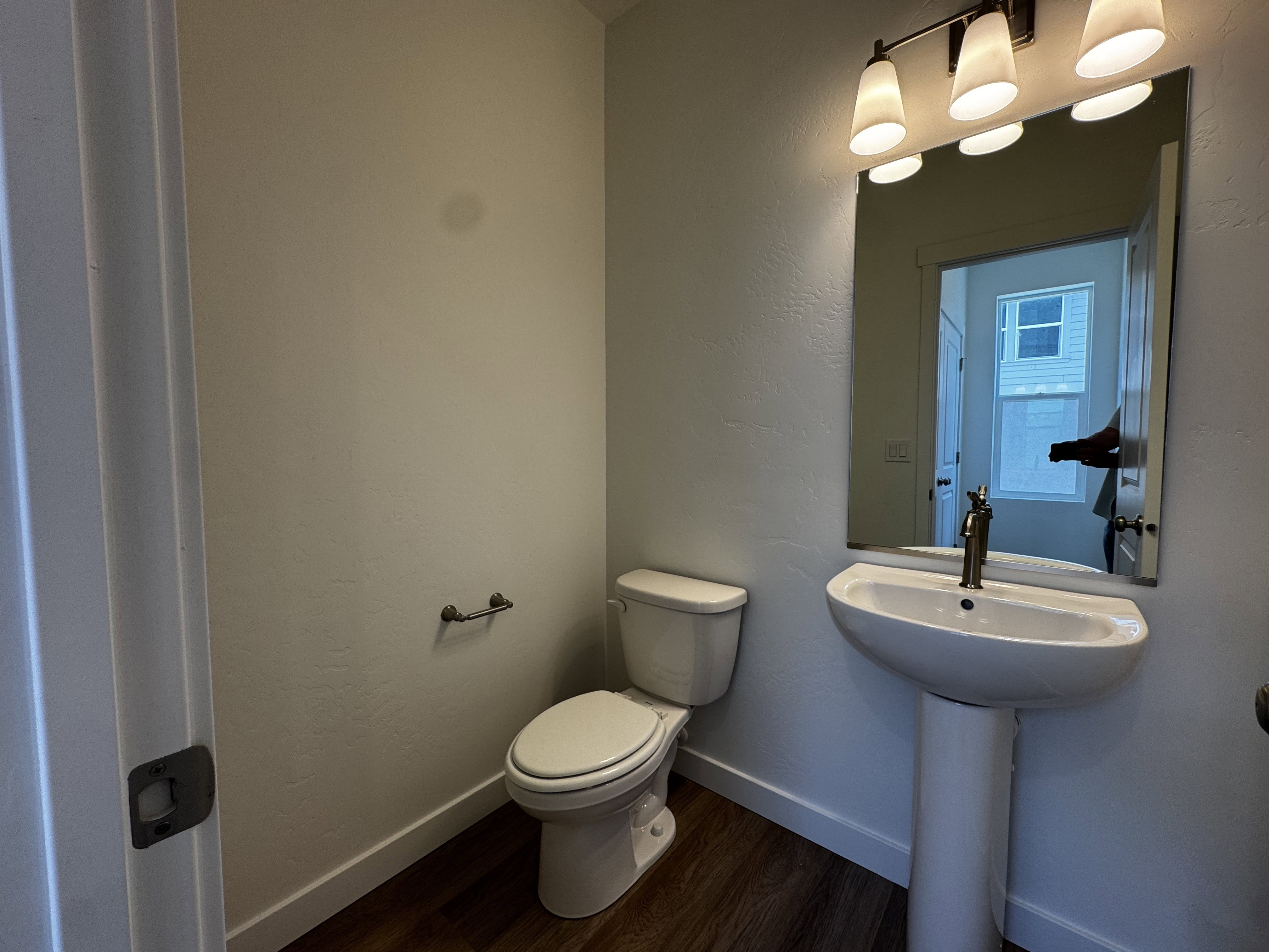 Pedestal sink with a bronze-finish faucet, rectangular mirror, and three-light vanity fixture
