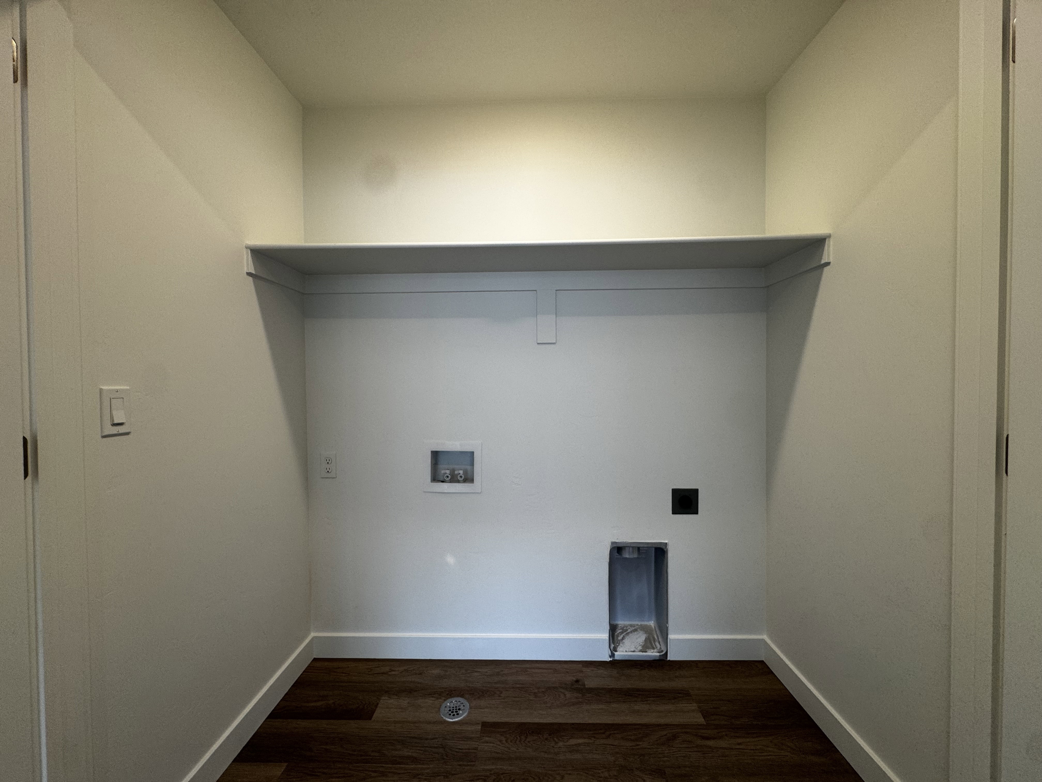 Dedicated laundry area featuring a built-in shelf, wood-finish flooring, white baseboards, and essential utility hookups