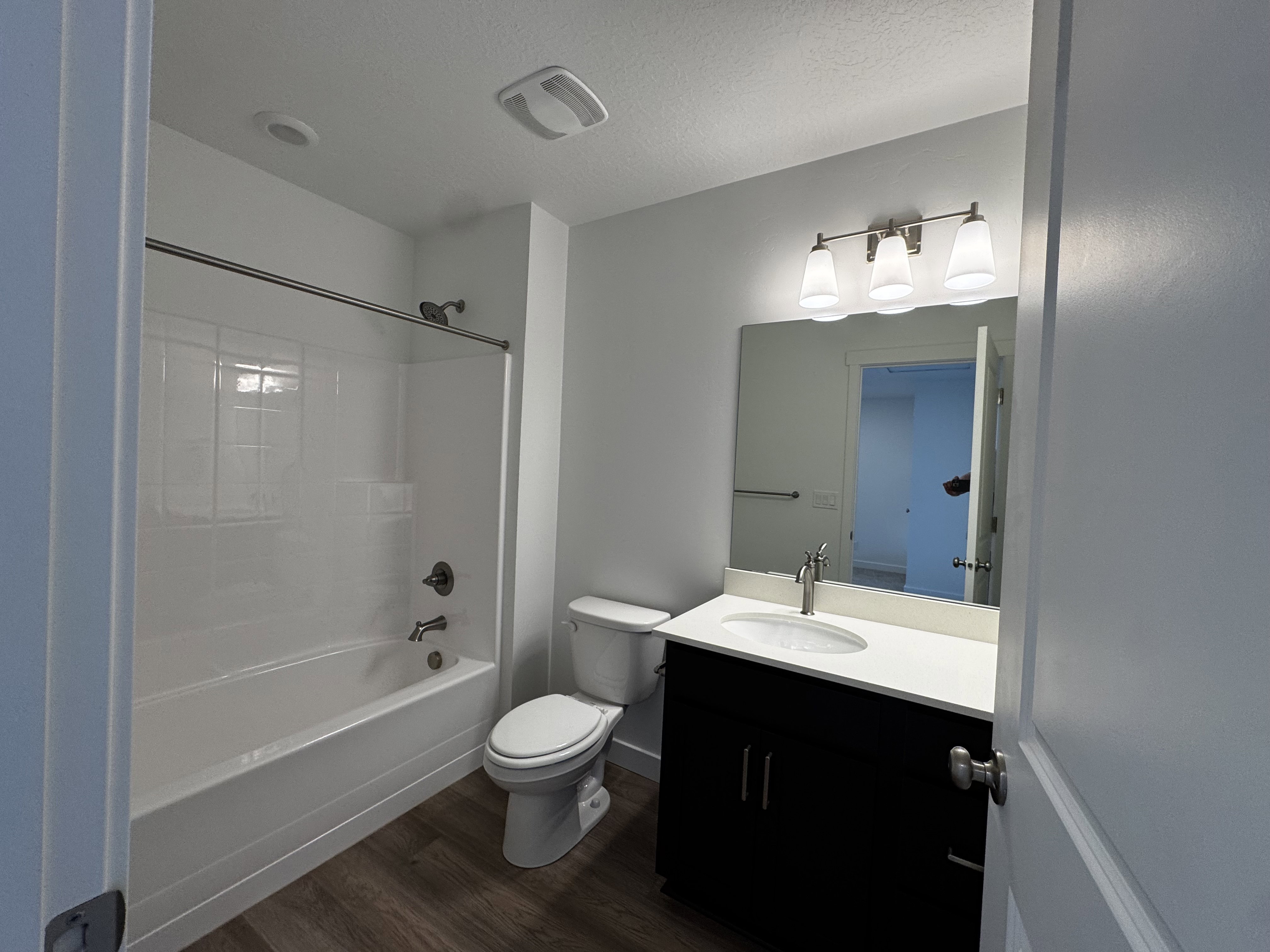 Bathroom featuring a tub/shower combination with white subway tile surround, dark wood-finish vanity with a white countertop and integrated sink, and wood-finish flooring