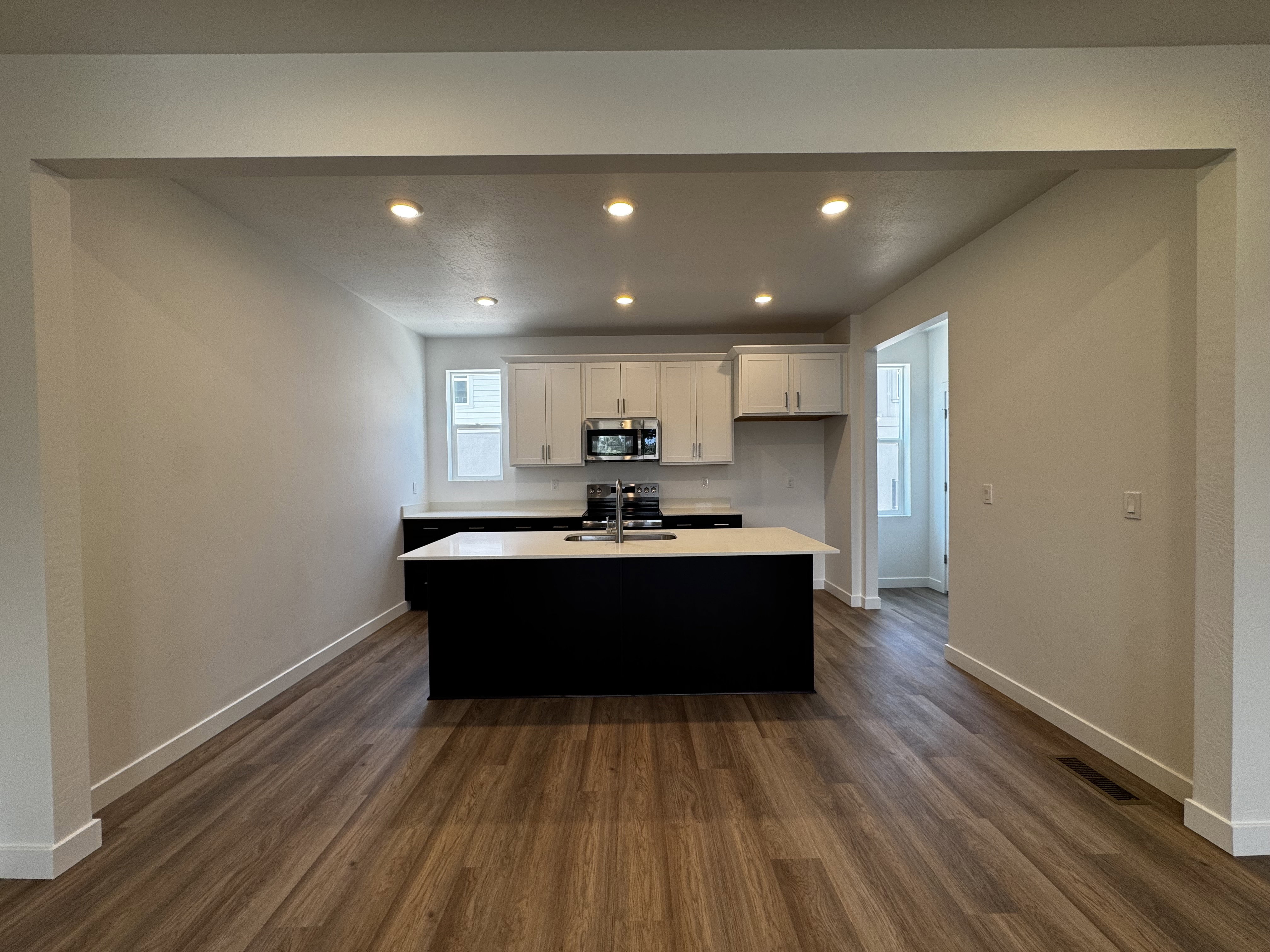 Open-concept kitchen featuring an island with a white countertop, white upper cabinetry, and stainless steel appliances