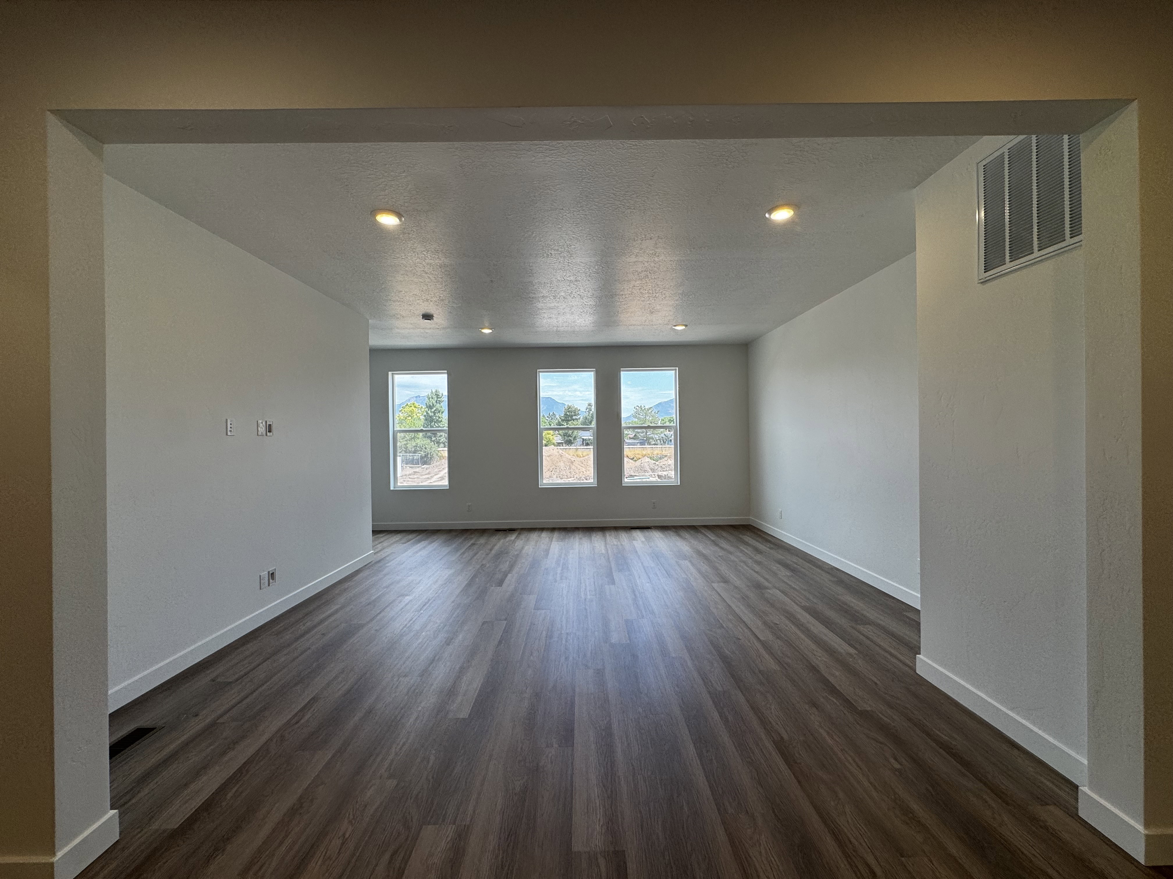 Spacious room featuring wood-finish flooring, white walls, and recessed lighting