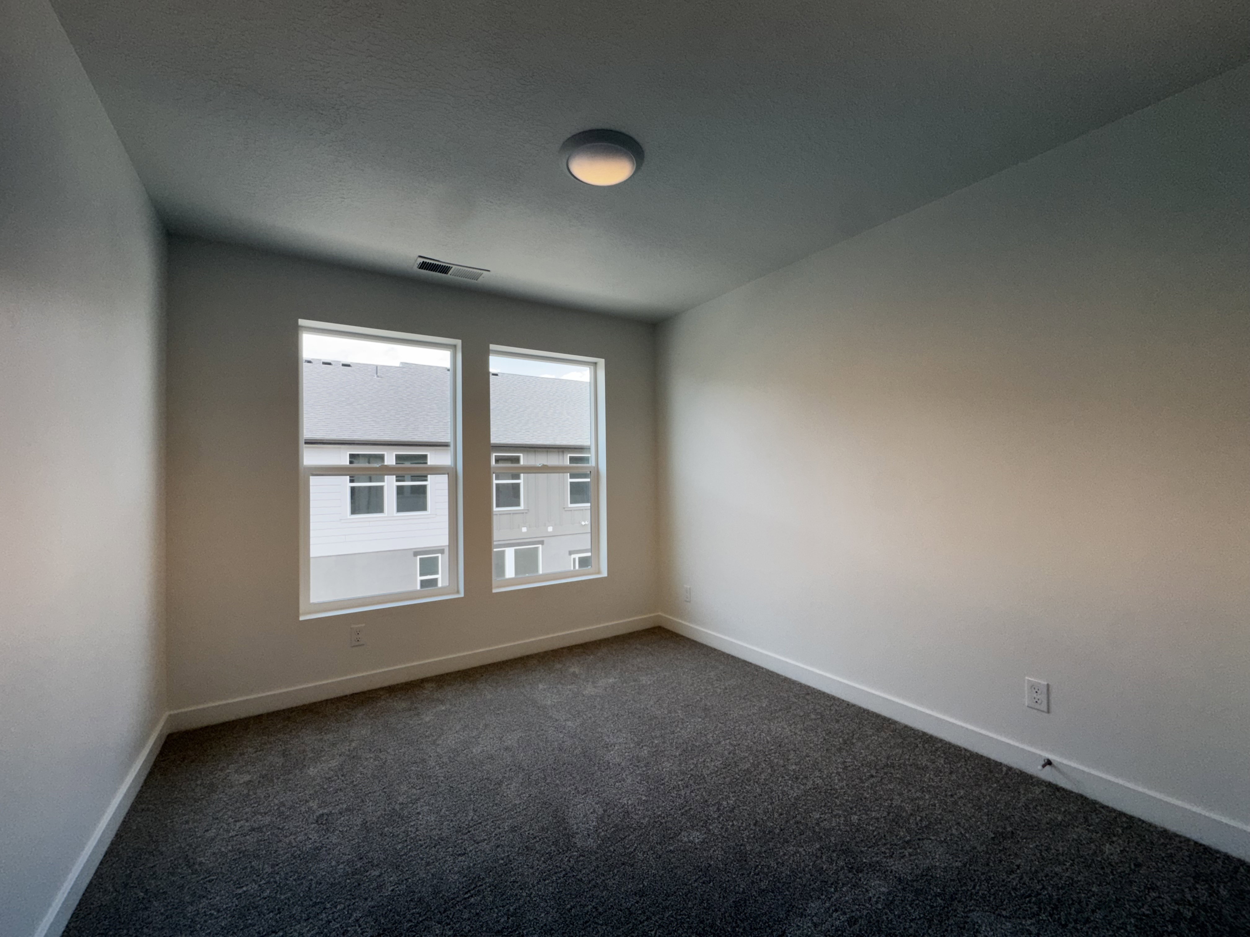 Room featuring two large windows, dark grey carpet, white baseboards, and a flush-mount ceiling light fixture