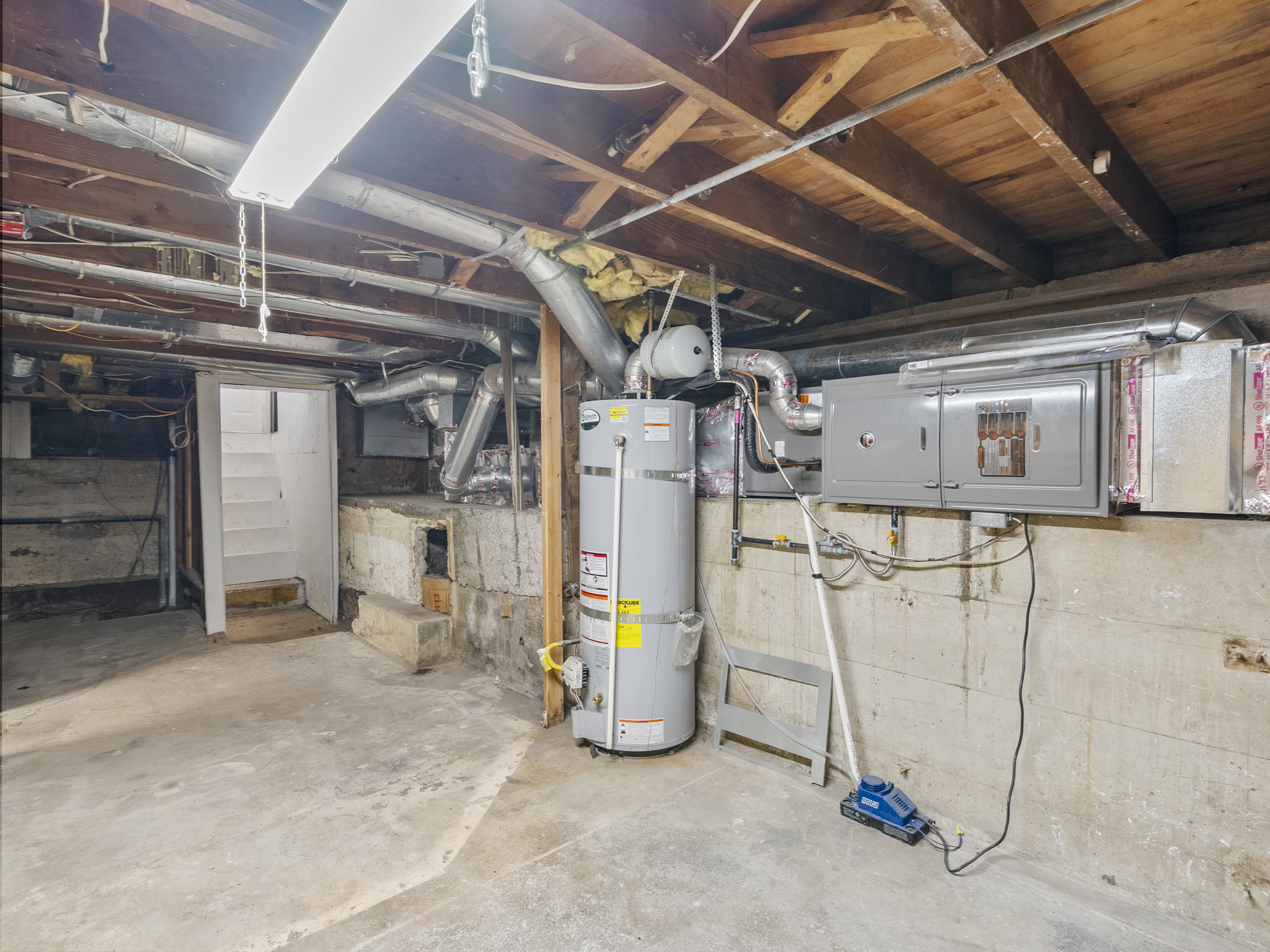 Basement utility area featuring a water heater, furnace, exposed wood beams, concrete flooring, and an accessible staircase