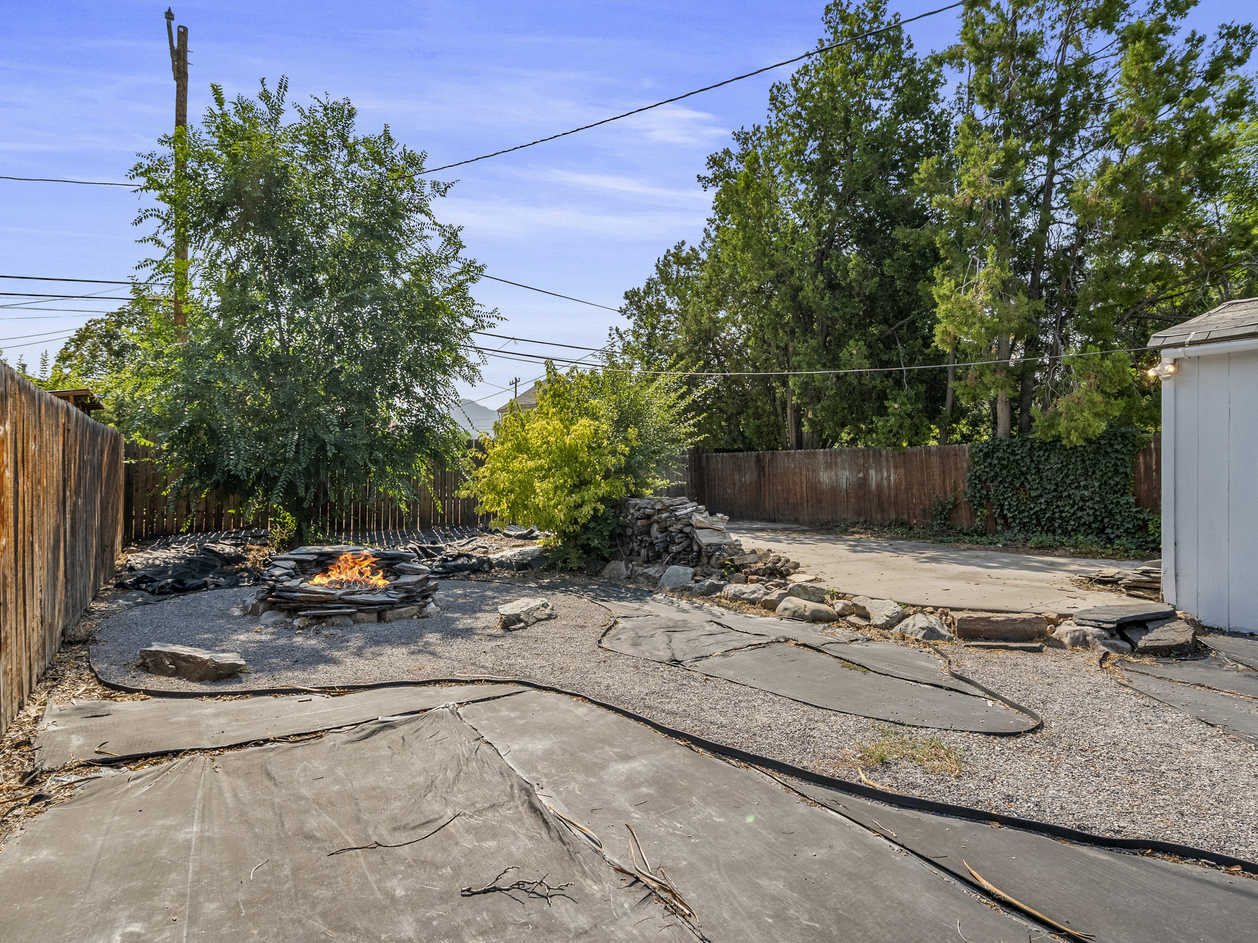 Outdoor space featuring a stone fire pit, gravel landscaping, and mature trees