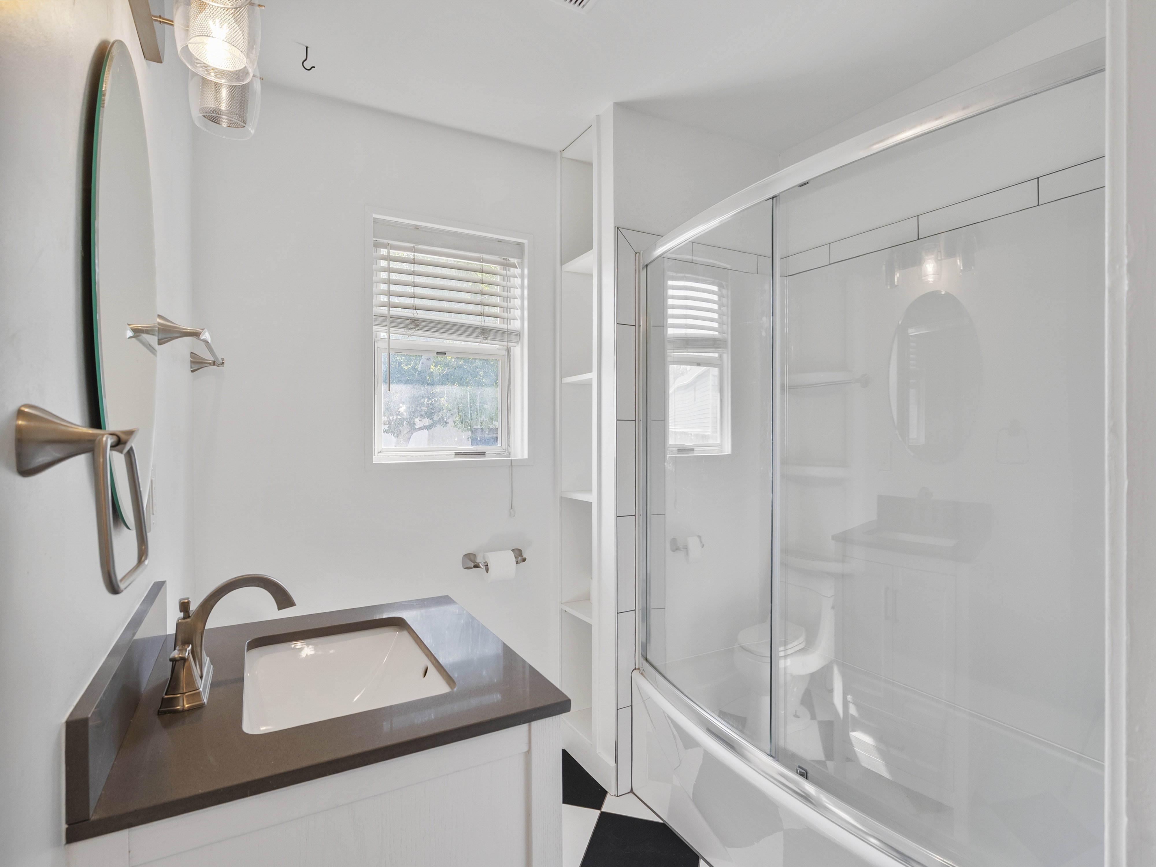 Bathroom featuring a built-in vanity with a dark countertop and undermount sink, a shower-tub combination with a sliding glass door, and a black and white checkered floor
