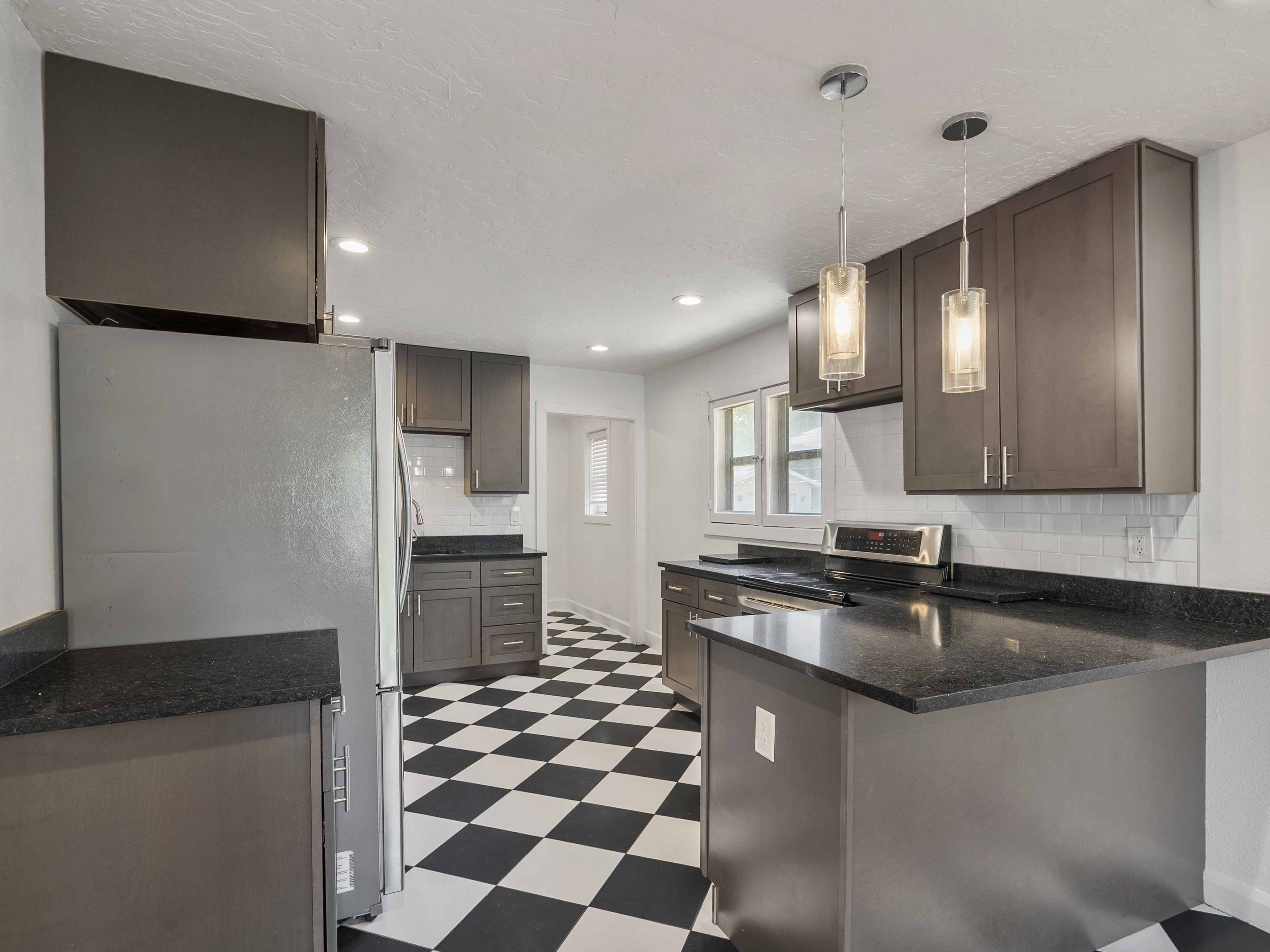 Kitchen featuring dark cabinetry, dark stone countertops, stainless steel appliances, a white subway tile backsplash, and checkerboard floor tiles