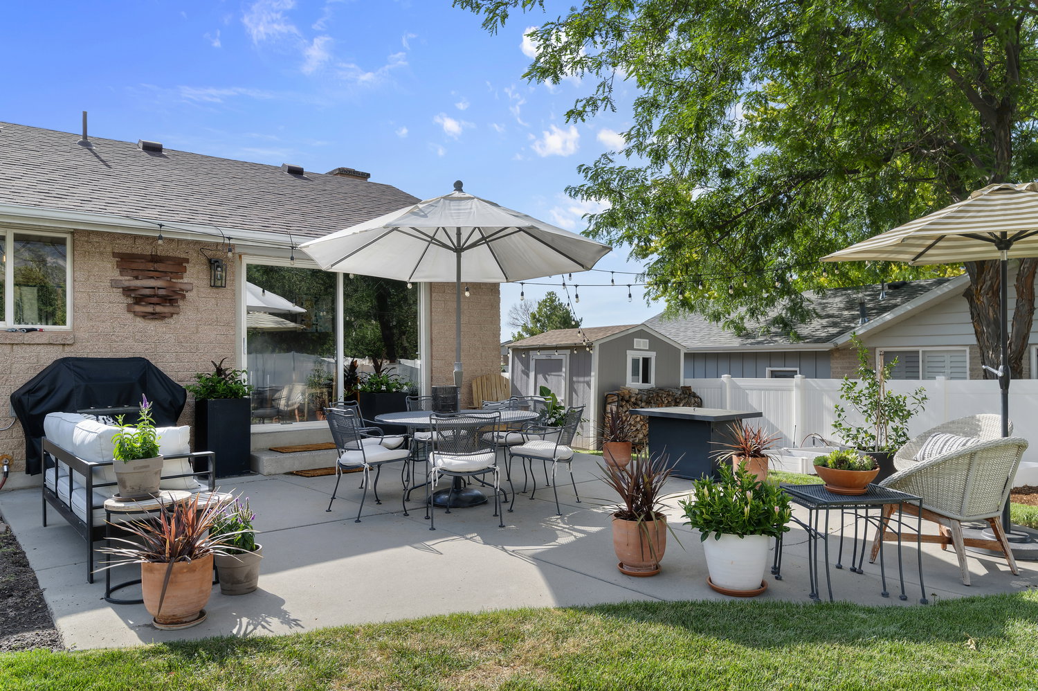 Expansive concrete patio with a detached storage shed, privacy fencing, and mature trees