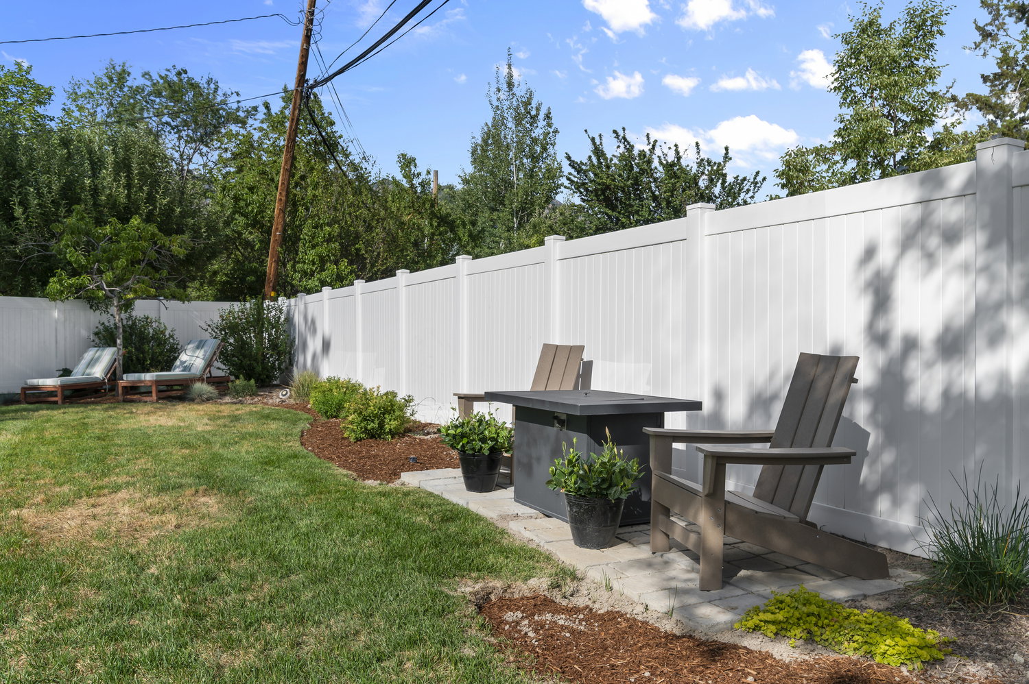 Expansive backyard featuring a manicured lawn, white privacy fencing, and mature perimeter trees