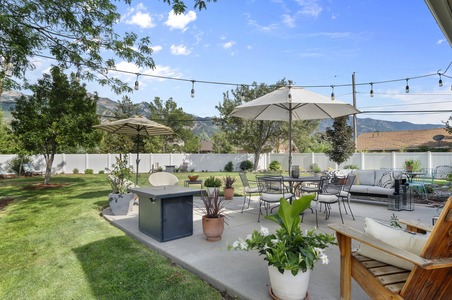 Expansive concrete patio featuring string lighting, a fire pit, and privacy fencing