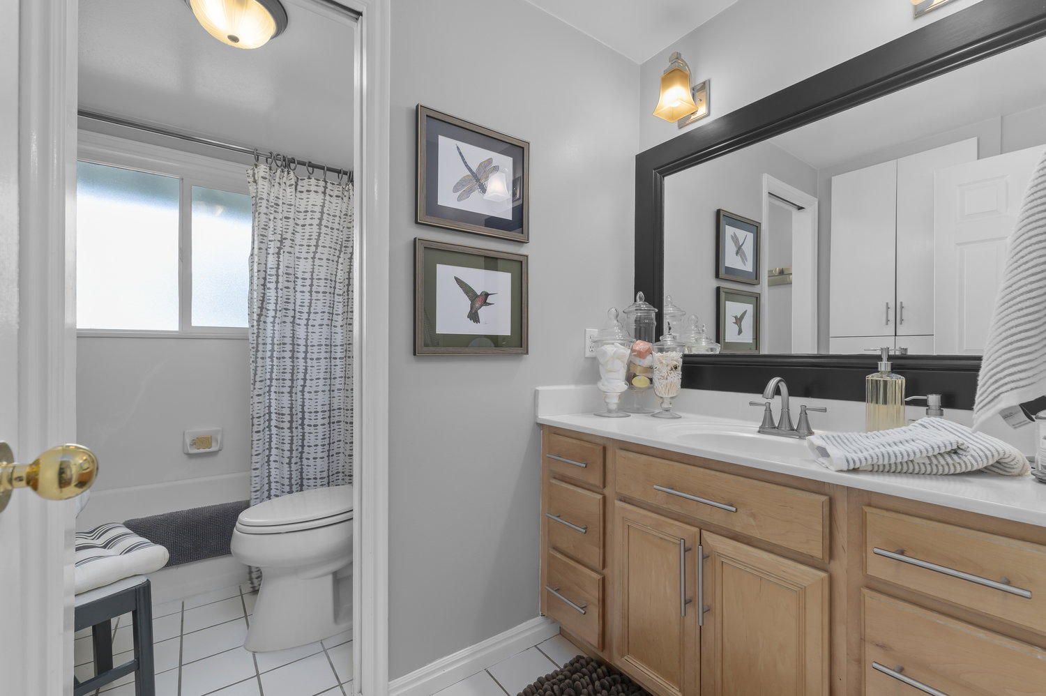 Bathroom featuring a natural wood-finish vanity with a white countertop and undermount sink, brushed nickel faucet, large framed mirror, and overhead vanity lighting