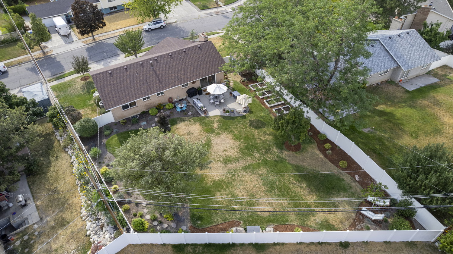 Expansive rear yard featuring a large patio, built-in garden beds, mature trees, and landscaping