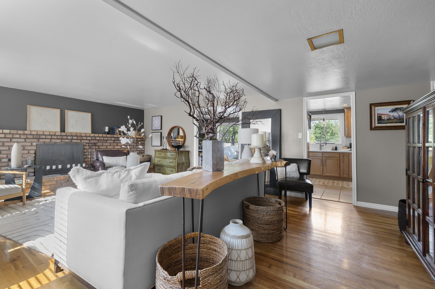 Sunlit living area featuring rich wood-finish flooring, a brick-faced fireplace, and a light gray accent wall