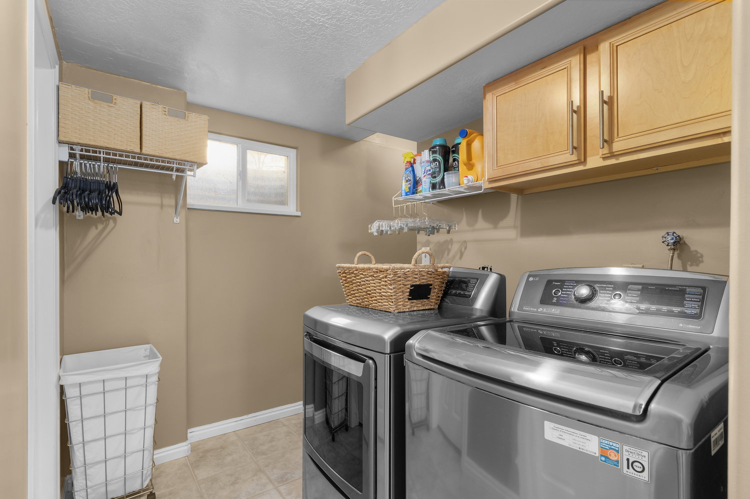 Dedicated laundry area featuring tile flooring, a horizontal window, light wood-finish cabinetry, and an upper wire shelf with hanging rod
