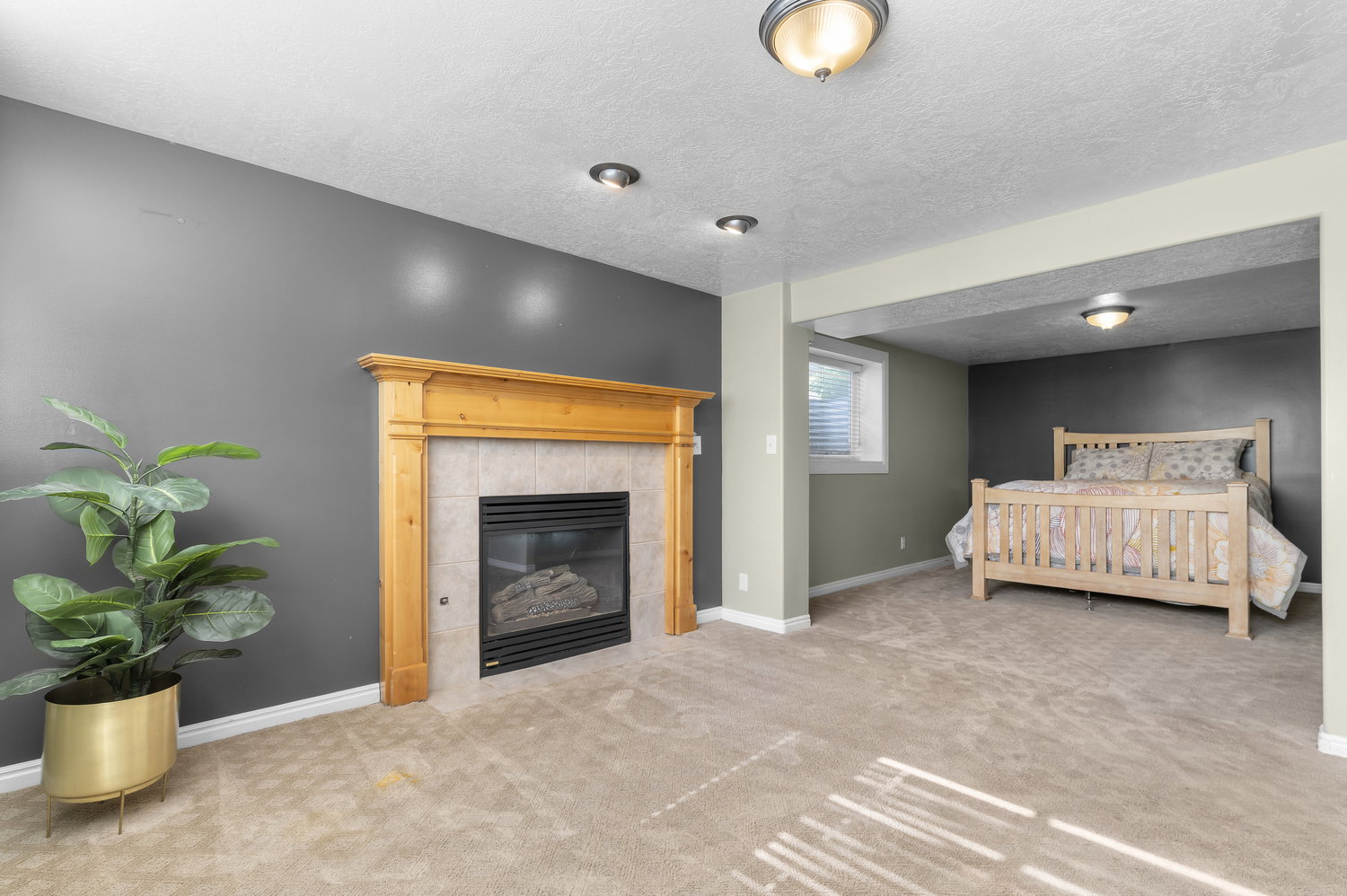 Carpeted room featuring a fireplace with a light wood mantel and tiled surround, recessed lighting, and a partially visible window with blinds