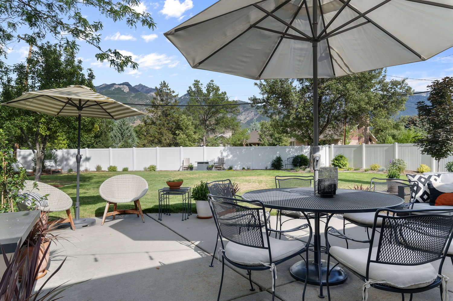 Expansive backyard featuring a large concrete patio, manicured lawn, and white privacy fencing
