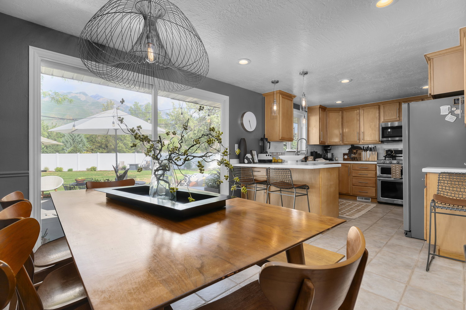 Spacious dining area with a contemporary wire pendant light and a large picture window overlooking a manicured backyard with mountain scenery