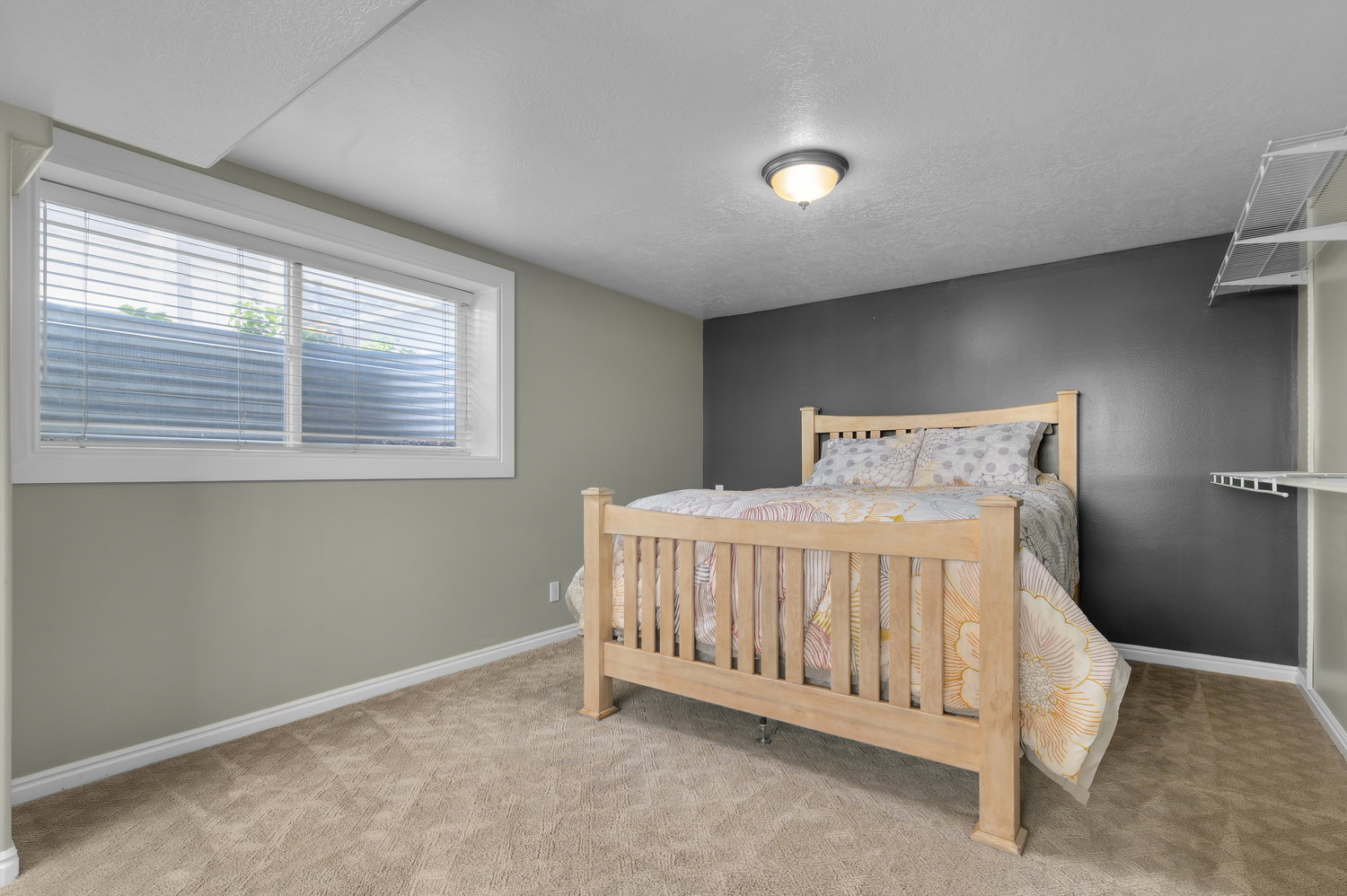 Carpeted room featuring a window with blinds, light green walls, a dark accent wall, and a ceiling-mounted light fixture