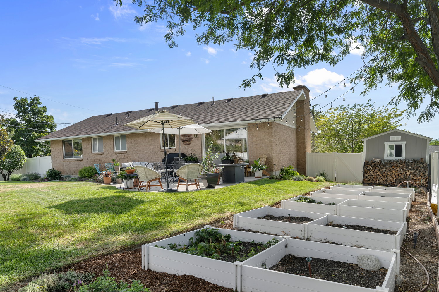 Expansive backyard featuring a brick exterior, a paved patio, a storage shed, and multiple raised garden beds