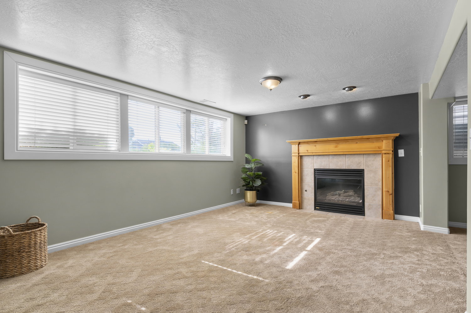 Carpeted interior space featuring a fireplace with a light wood mantel and tile surround, recessed lighting, and a horizontal window array with blinds