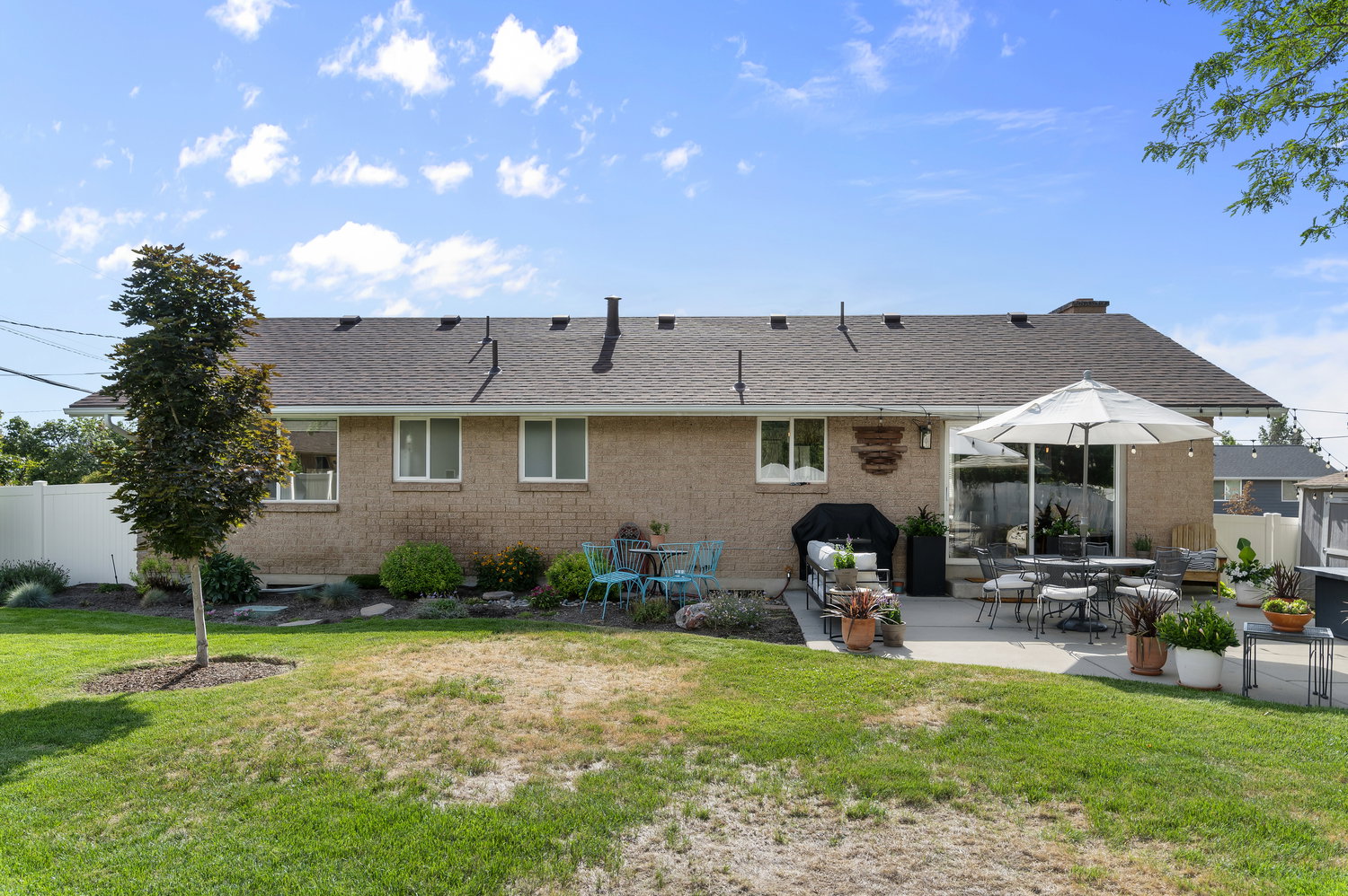 Expansive backyard featuring a large concrete patio, mature tree, and a white privacy fence