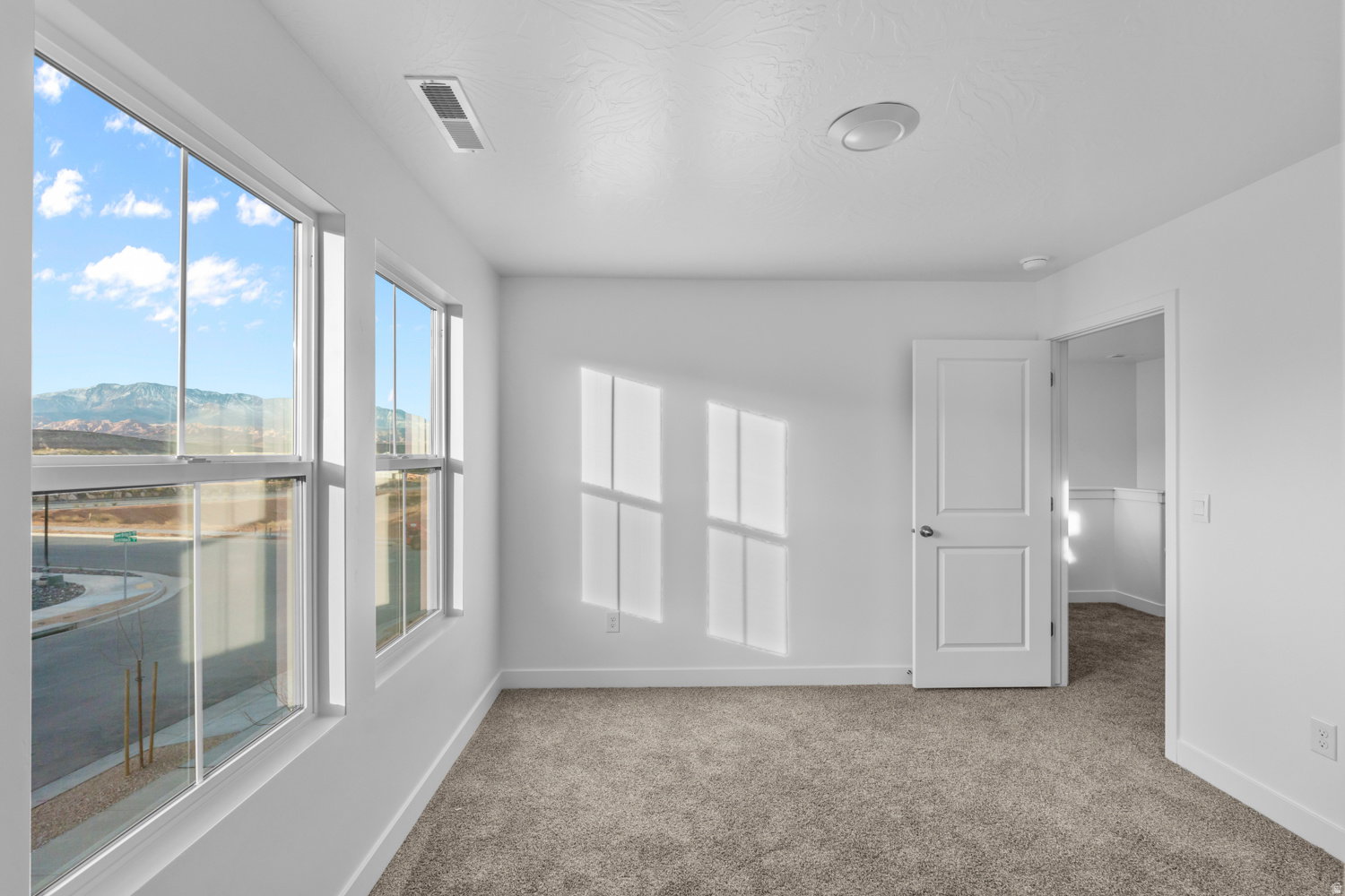Expansive windows framing a mountain backdrop, complemented by clean white walls, neutral carpet, a modern flush-mount ceiling light, and a contemporary two-panel interior door