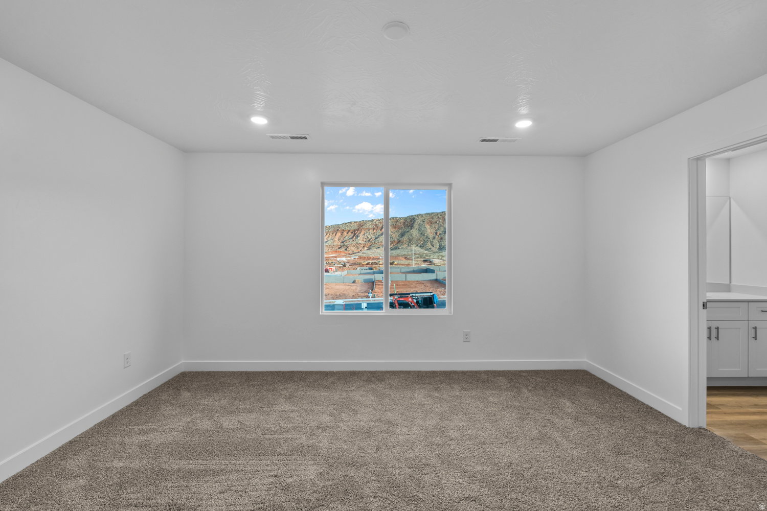Carpeted interior space featuring a window with a mountain backdrop, white walls, recessed lighting, and an entryway with wood-finish flooring