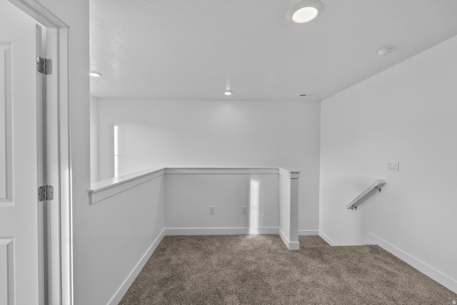 Carpeted landing area featuring a white railing, recessed lighting, and a white wall-mounted handrail