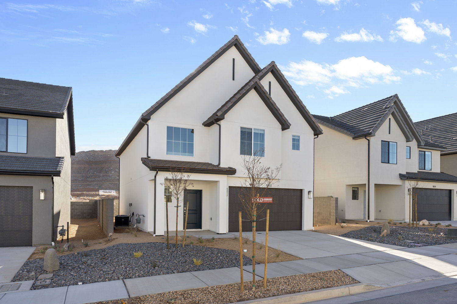 Modern two-story stucco residence featuring a dark tile roof, an integrated garage, a covered front entry, and xeriscape landscaping