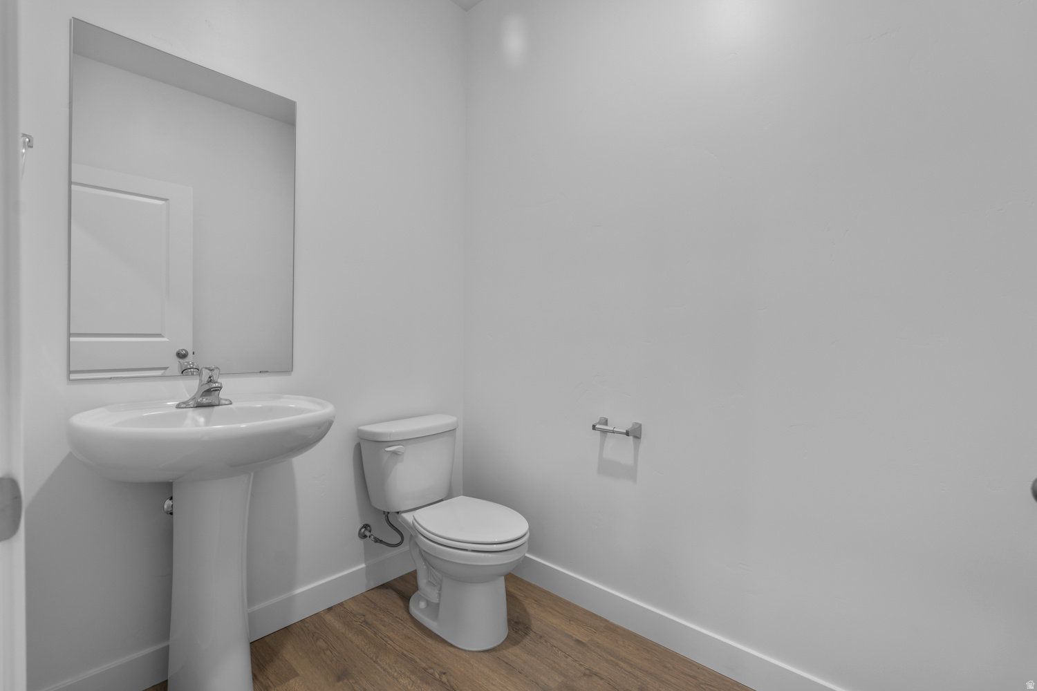 Powder room featuring a pedestal sink with a chrome faucet, a rectangular wall mirror, and wood-finish flooring