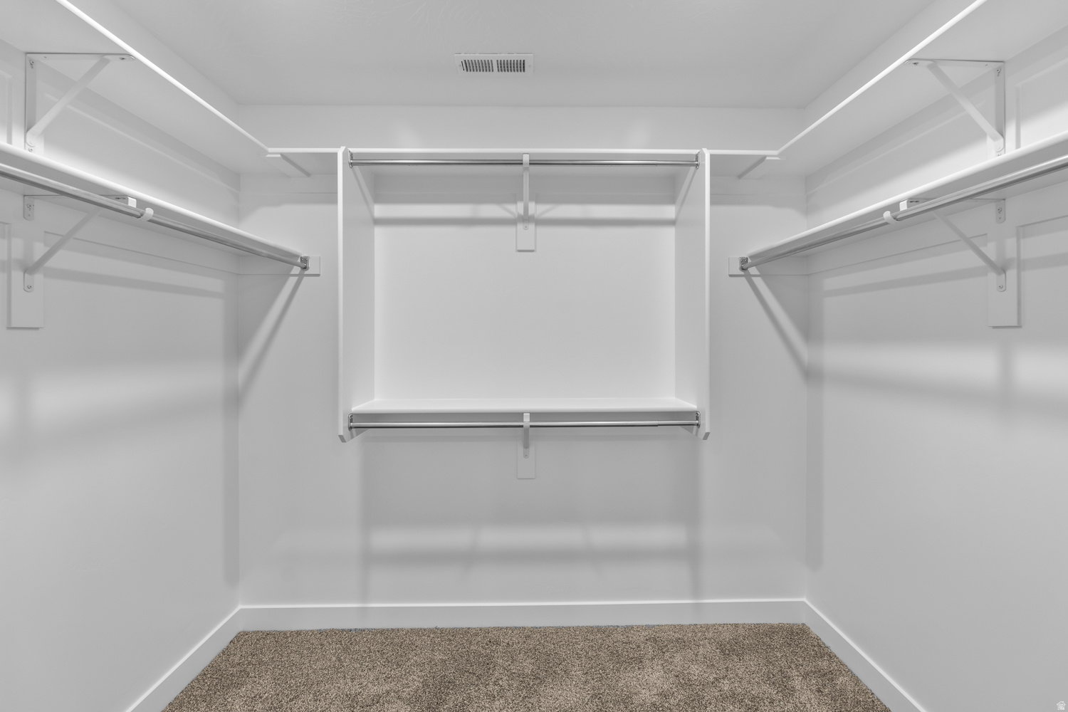 Walk-in closet featuring white shelving and hanging rods, white baseboards, and carpeted flooring