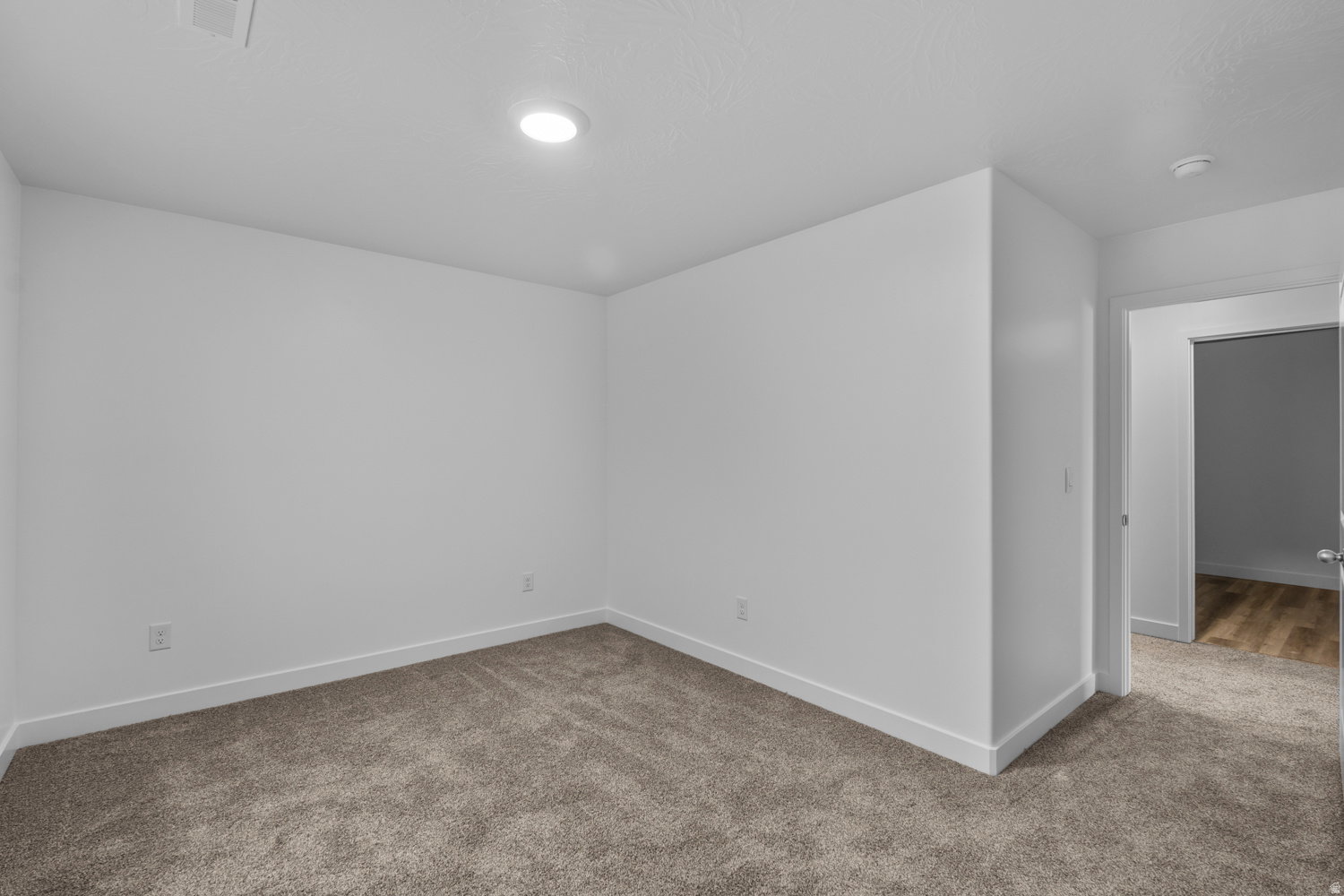 Spacious interior room featuring plush carpeting, crisp white walls, and recessed ceiling lighting
