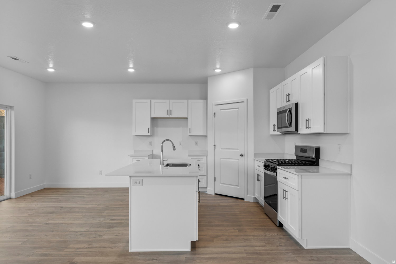 Modern kitchen featuring an island with a stainless steel sink, white cabinetry, integrated microwave, gas range, and wood-finish flooring
