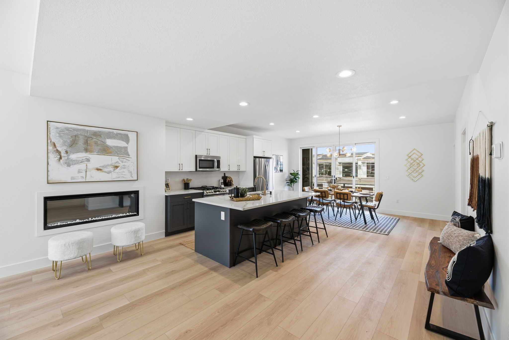 Open-concept living space featuring wood-finish flooring, a linear electric fireplace, a kitchen island with seating, white upper cabinetry, and stainless steel appliances