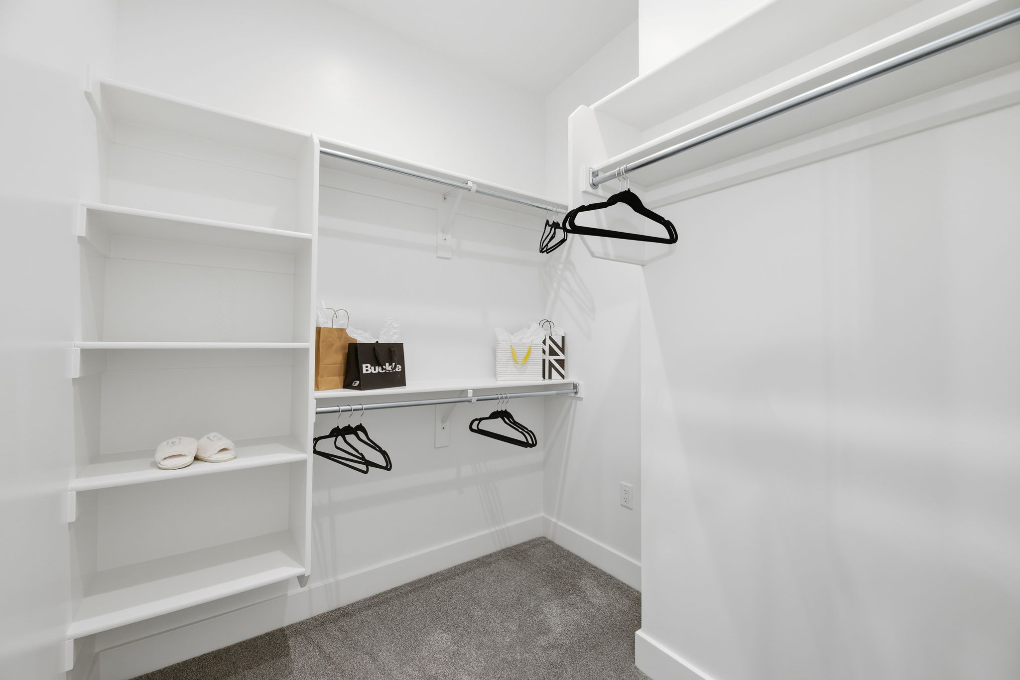 Walk-in closet featuring white built-in shelving, white walls, gray carpet, and multiple clothing rods