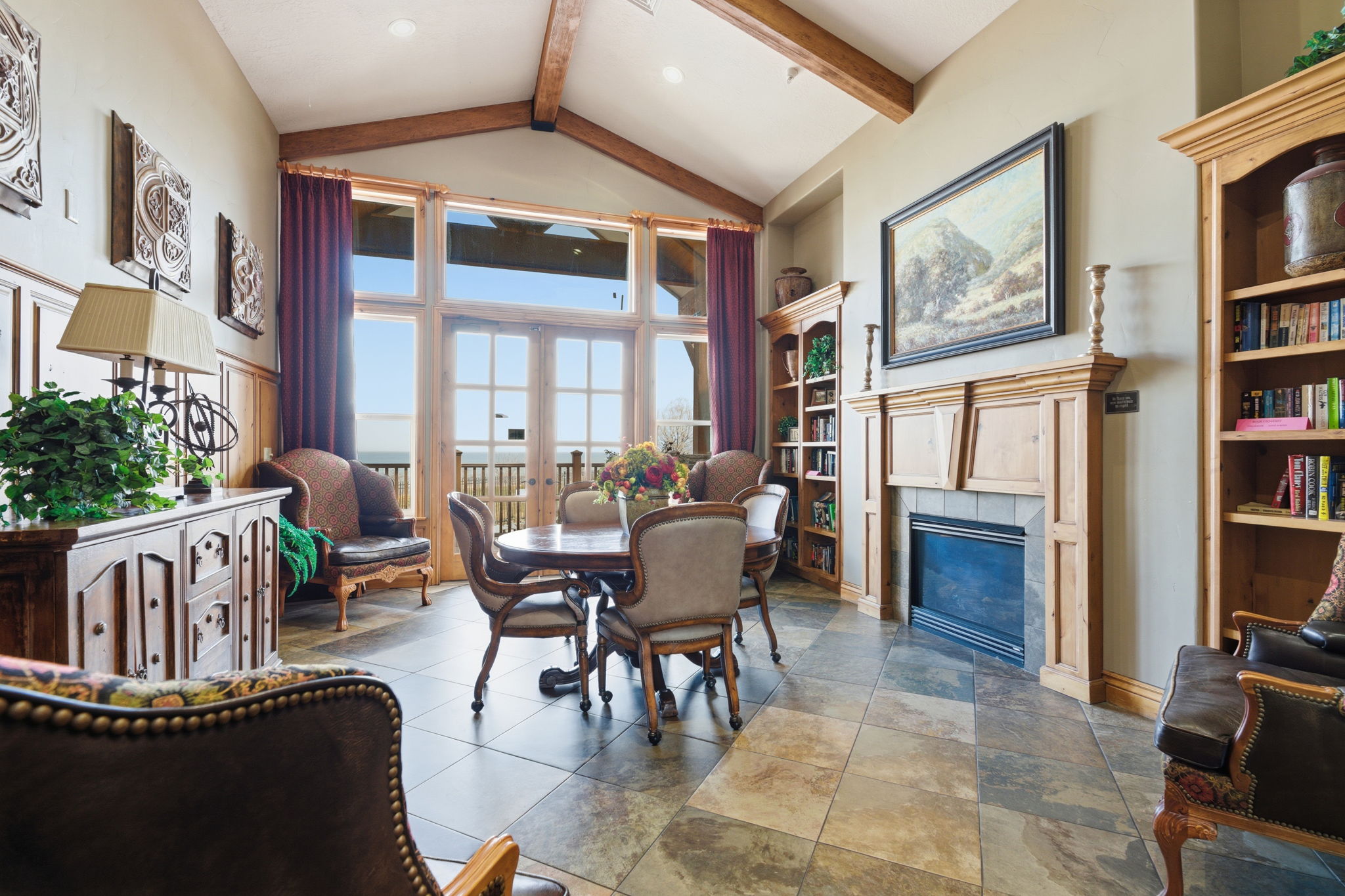 Vaulted ceilings with exposed wood beams highlight this living space featuring extensive window and door openings, providing abundant natural light