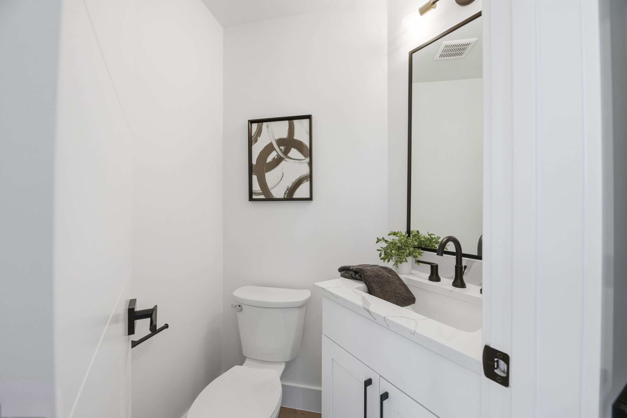 Powder room featuring a white single-sink vanity with a light-toned countertop, matte black faucet, and rectangular mirror with a dark frame
