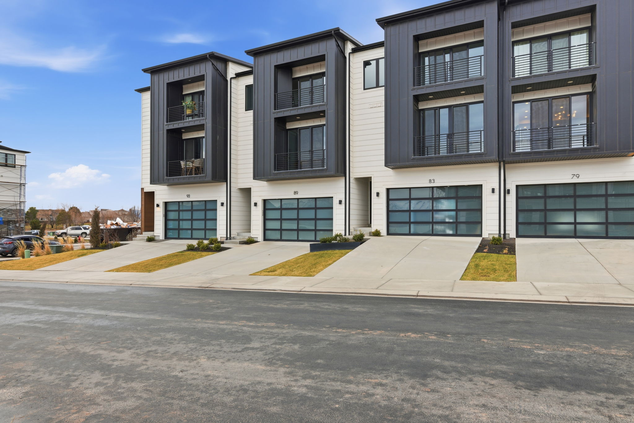 Modern townhome exterior showcasing a multi-level design, white horizontal siding, dark vertical panel accents, and glass panel garage doors