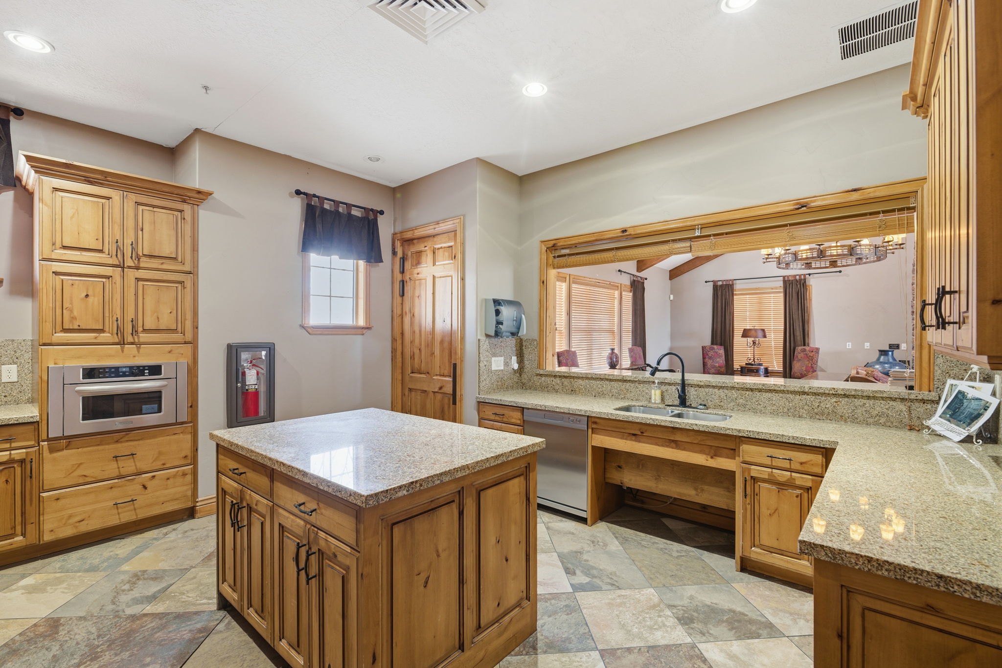 Kitchen featuring extensive wood cabinetry, granite countertops, a central island, built-in stainless steel microwave, and stone tile flooring