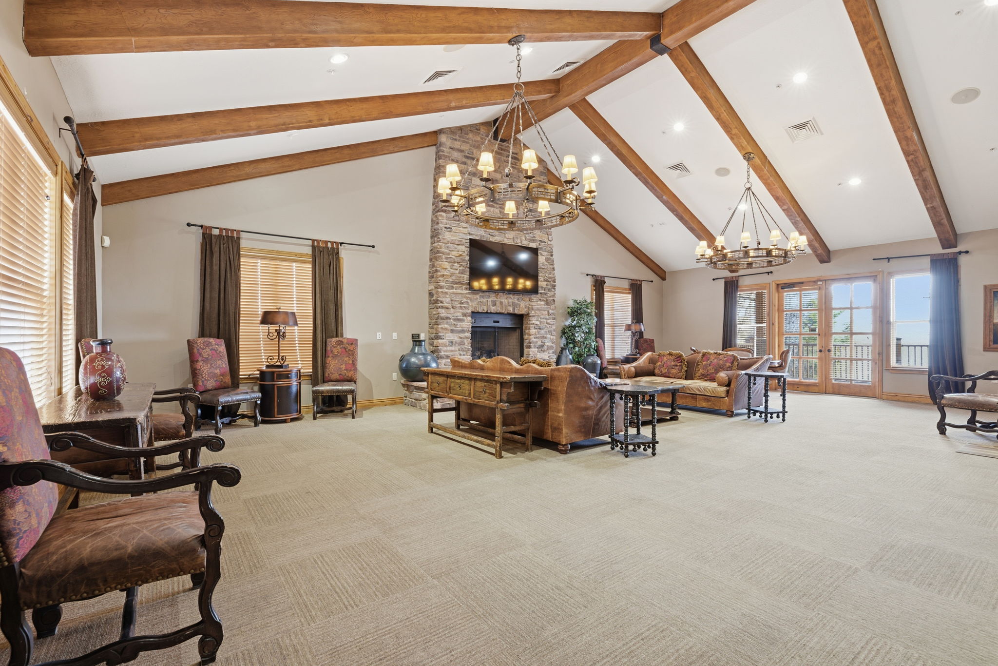 Spacious living area featuring a vaulted ceiling with exposed wood beams, a stone-clad fireplace, and multiple sets of French doors