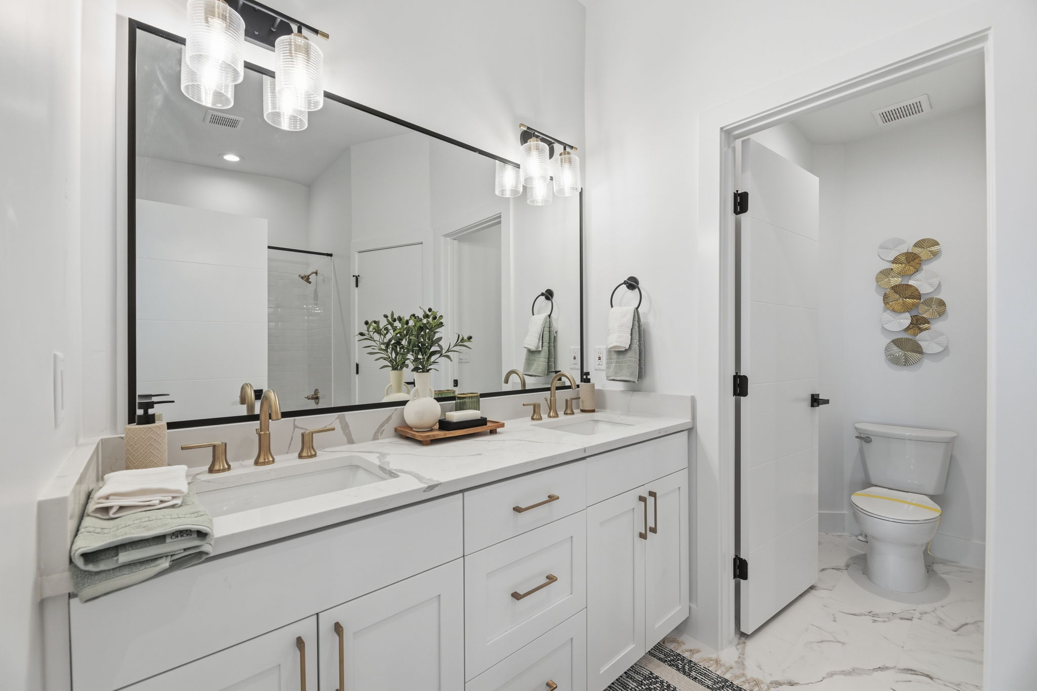 Spacious bathroom featuring a double vanity with white cabinetry, gold-tone hardware, and an expansive mirror