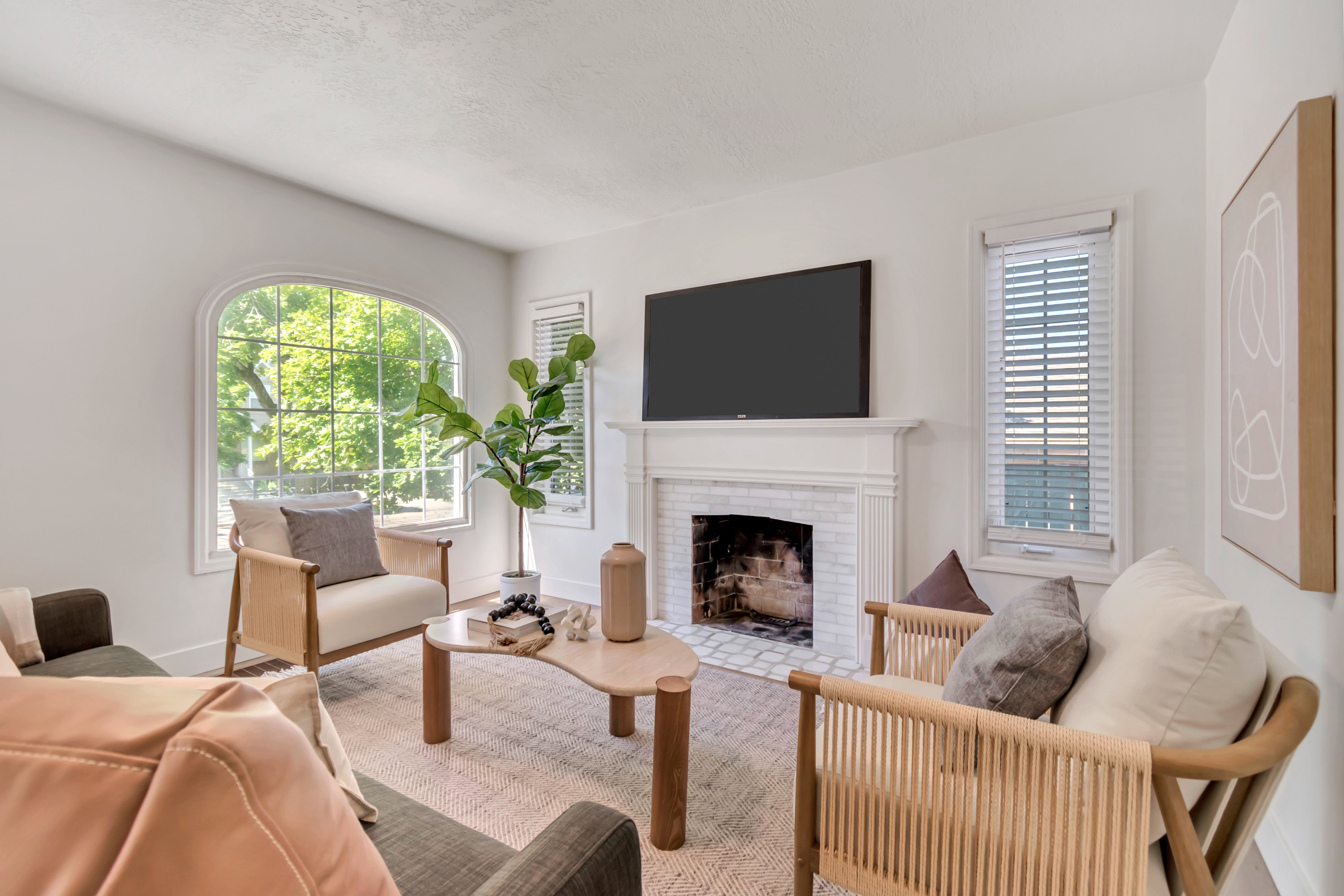 Living area featuring a white brick fireplace with a classic mantel, an arched window, white walls, and wood-finish flooring with an area rug