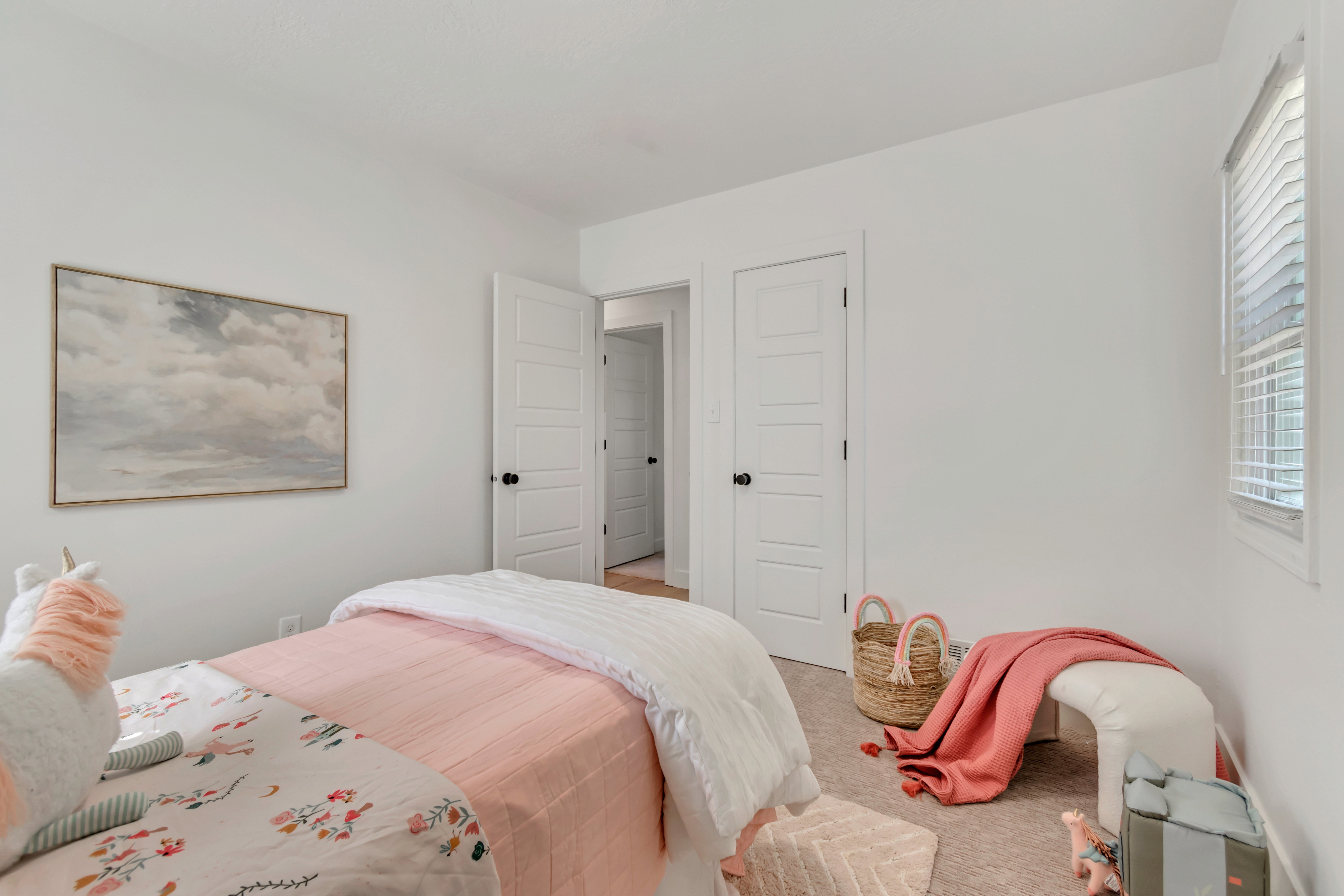 Bright room featuring a window with blinds, light-colored carpeting, white walls, and white paneled doors with dark hardware