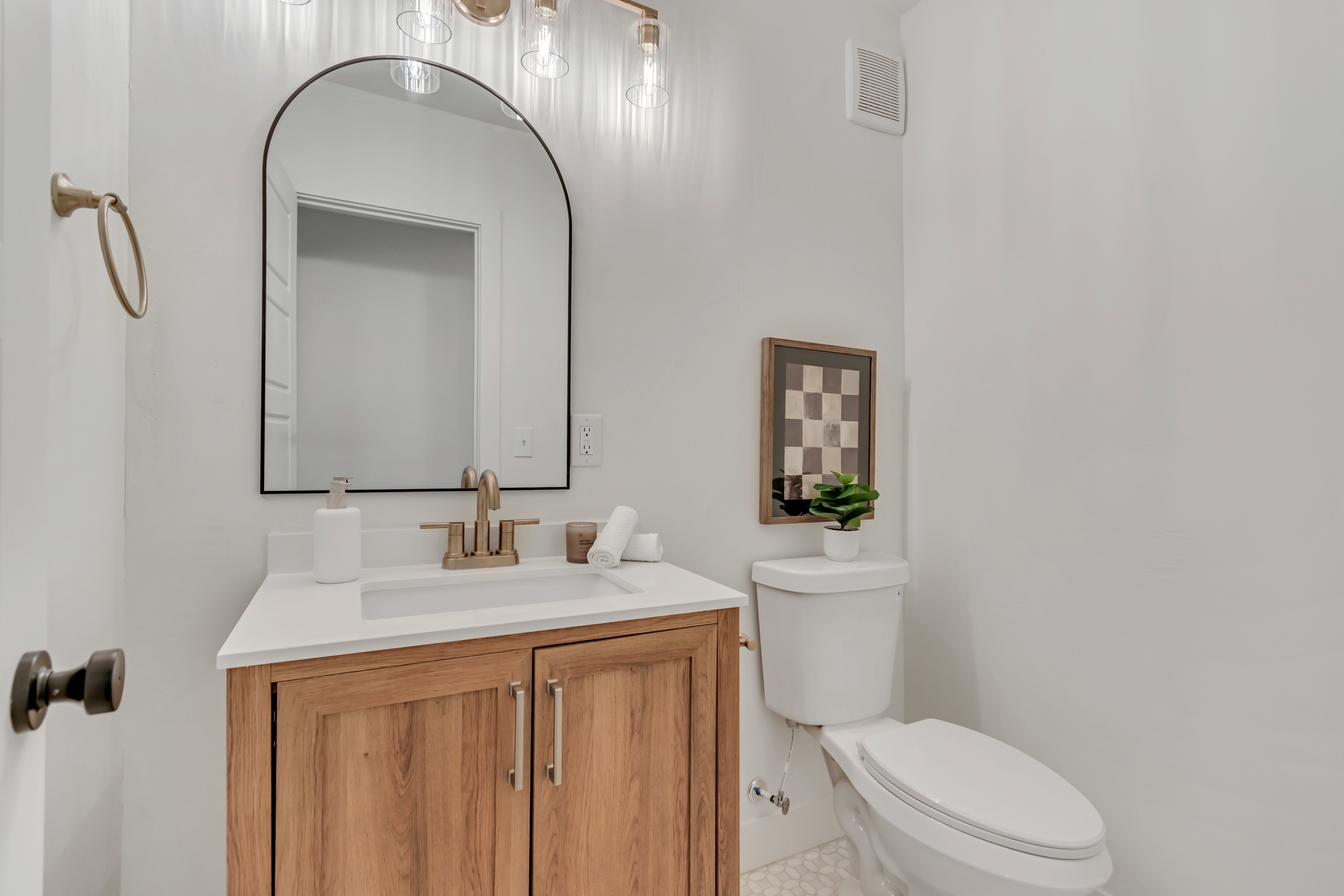 Bathroom featuring a wood-finish vanity with a white countertop, an arched mirror, and a modern light fixture